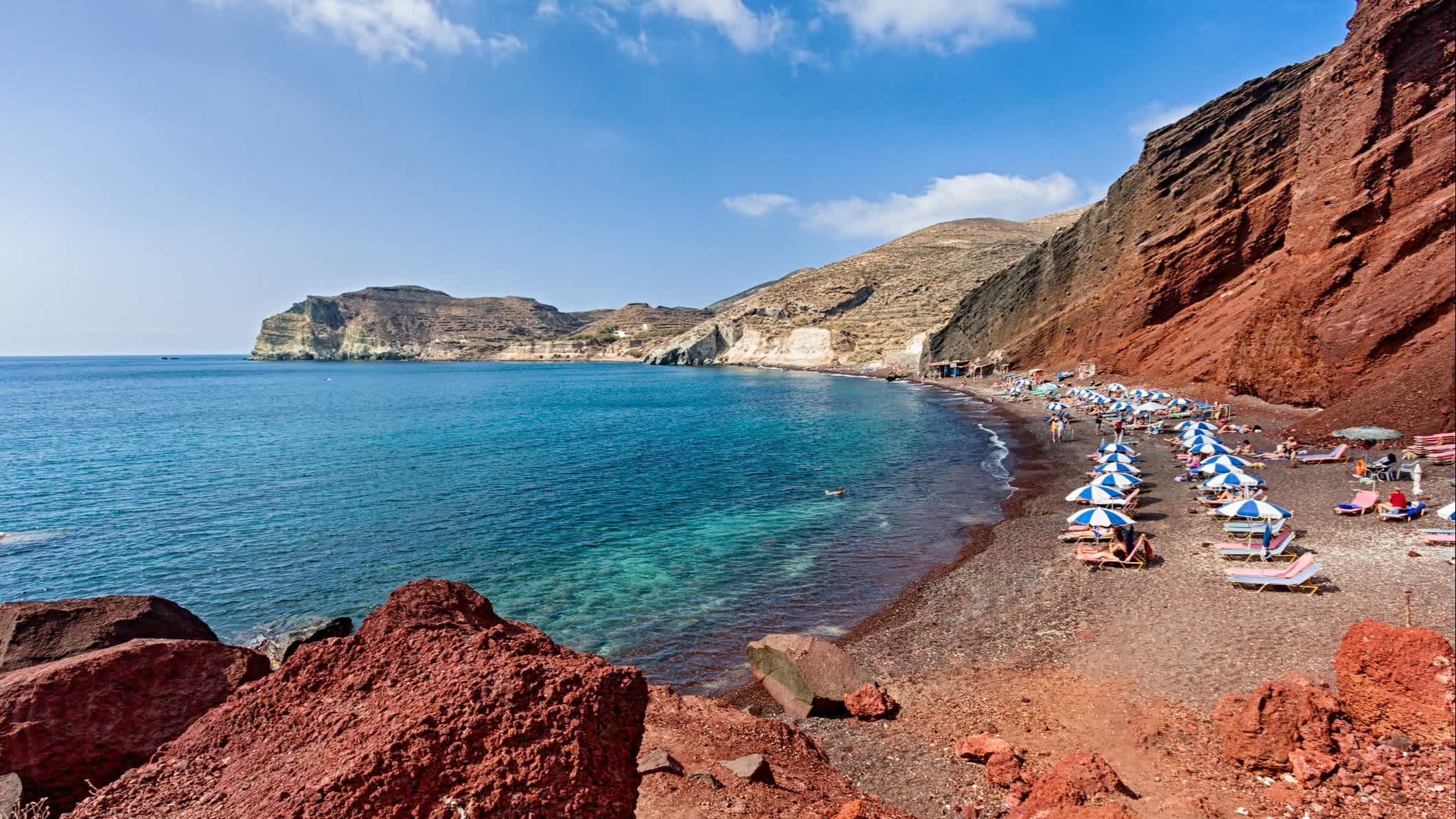 Transats et parasols sur la plage rouge, à Santorin, en Grèce.

