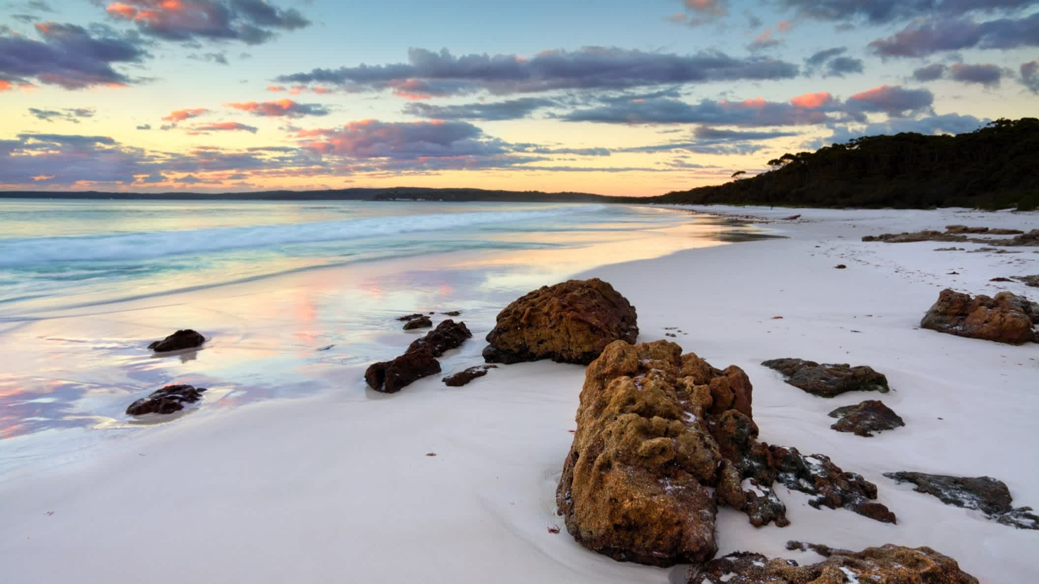 Der Sonnenaufgang am Hyams Beach, Australien mit Blick auf das Meer und Felsen im Bild.
