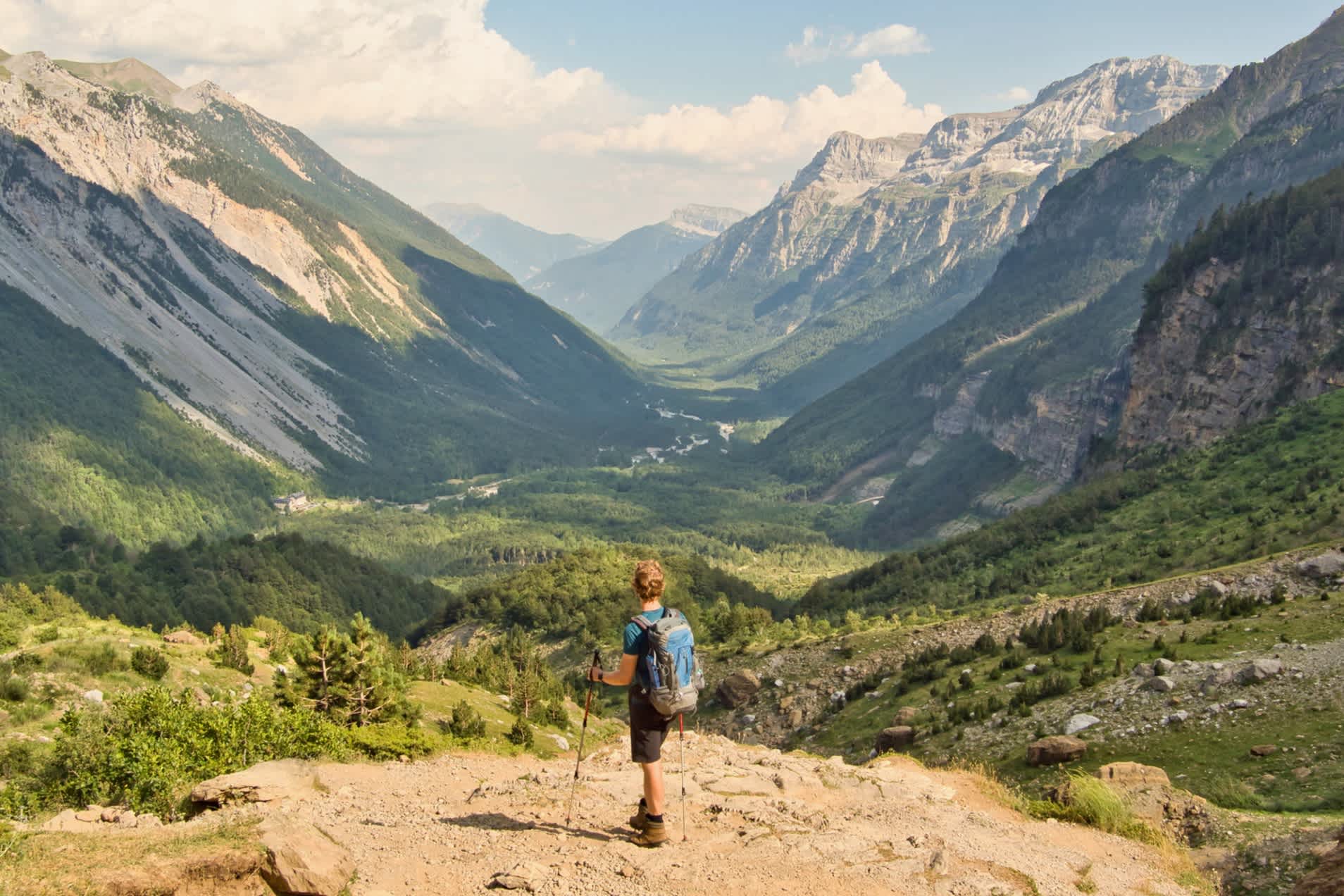 Mann mit Wanderstöcken blickt auf ein Tal zwischen majestätischen Bergen
