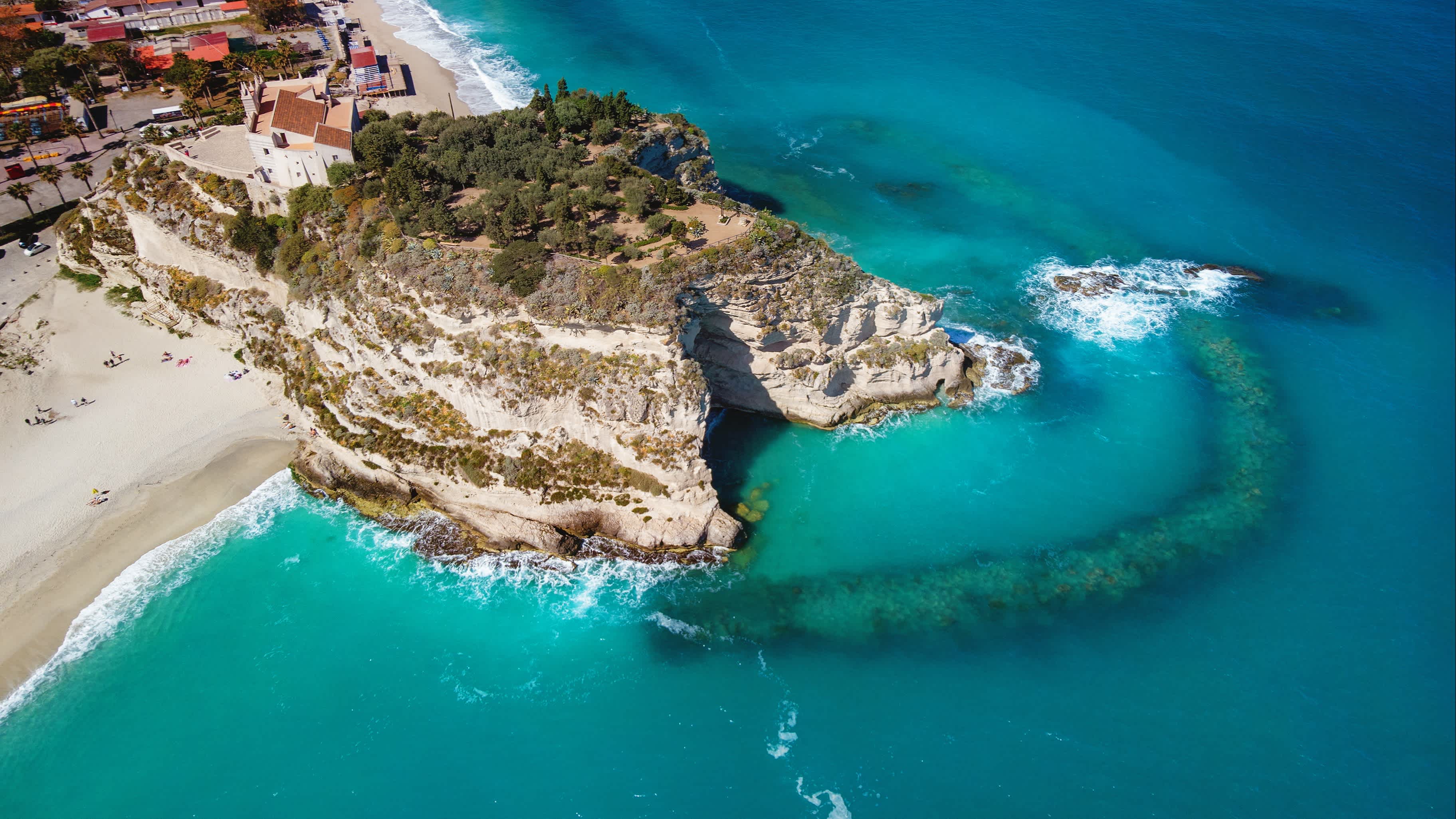 Atemberaubende Aufnahme des Strandes von Santa Maria dell'Isola, Kalabrien, mit türkisblauem Meer, Felsenbucht und Kirche.