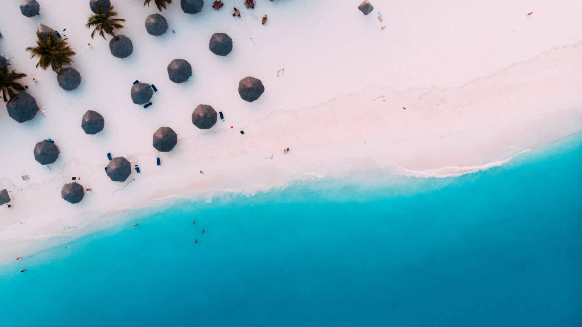 Luftaufnahme des tropischen Sandstrands Kendwa Beach auf Sansibar mit türkisblauem Meer, Sonnenschirmen und Palmen.