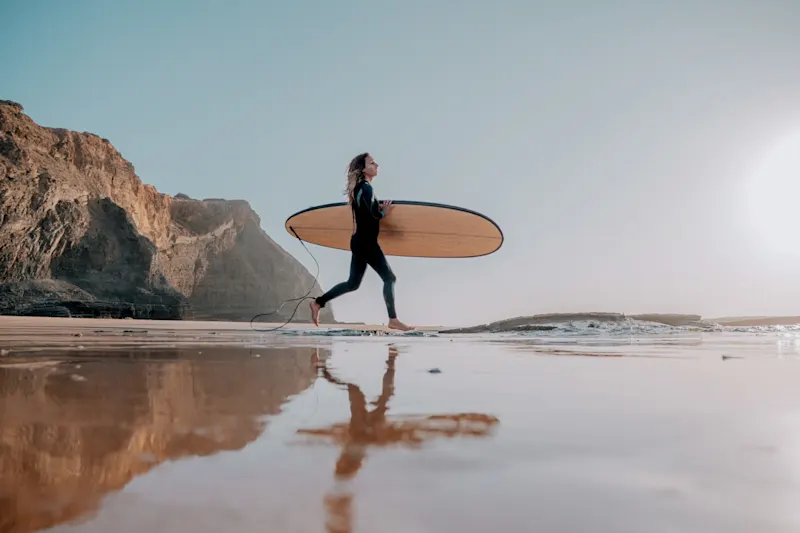 Surfer walking along the beach with a surfboard, Lagos, Algarve, Portugal.