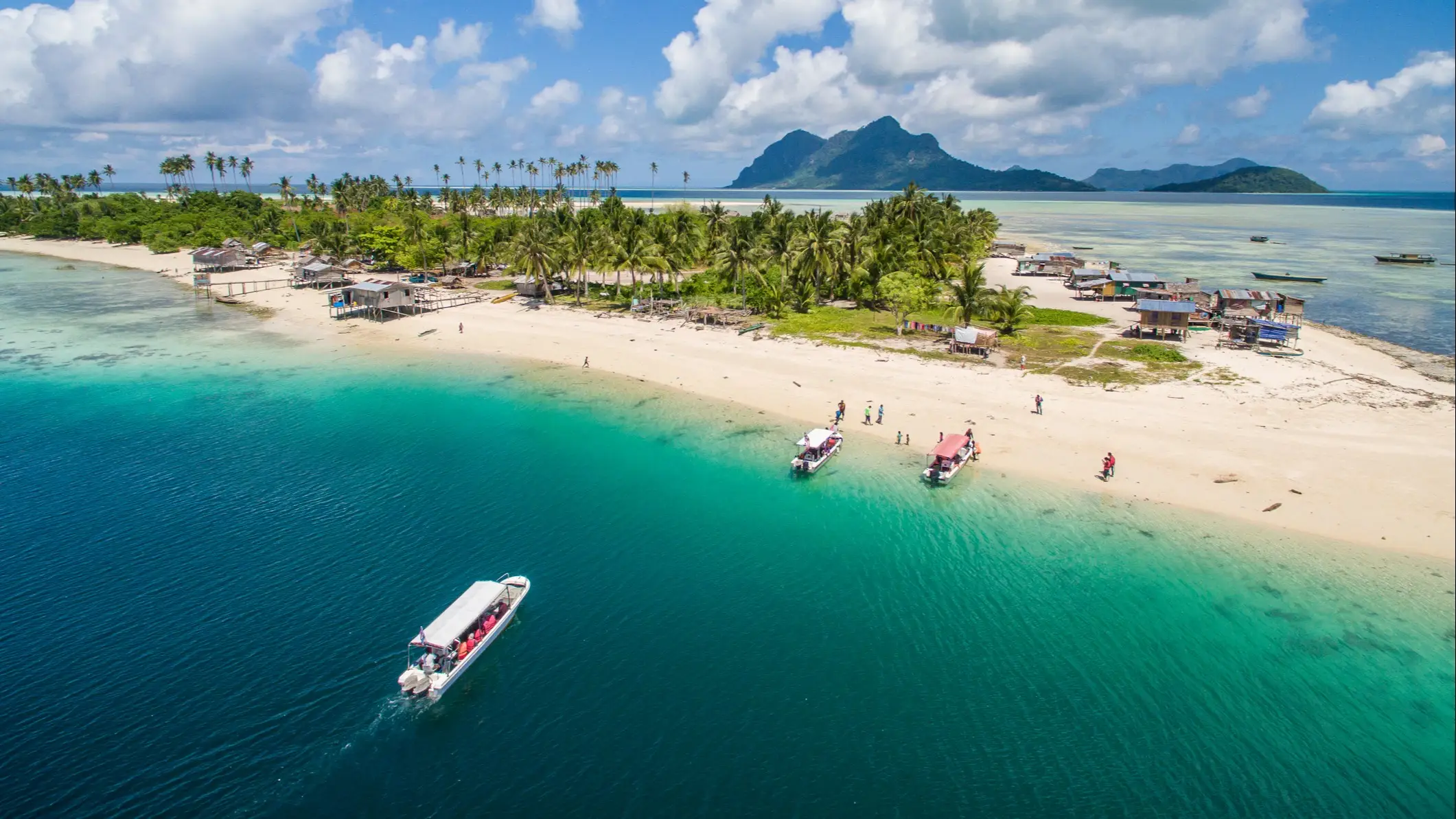 Tropische Insel mit Palmen und Booten am klaren, türkisfarbenen Wasser, Pulau Sipadan, Malaysia.