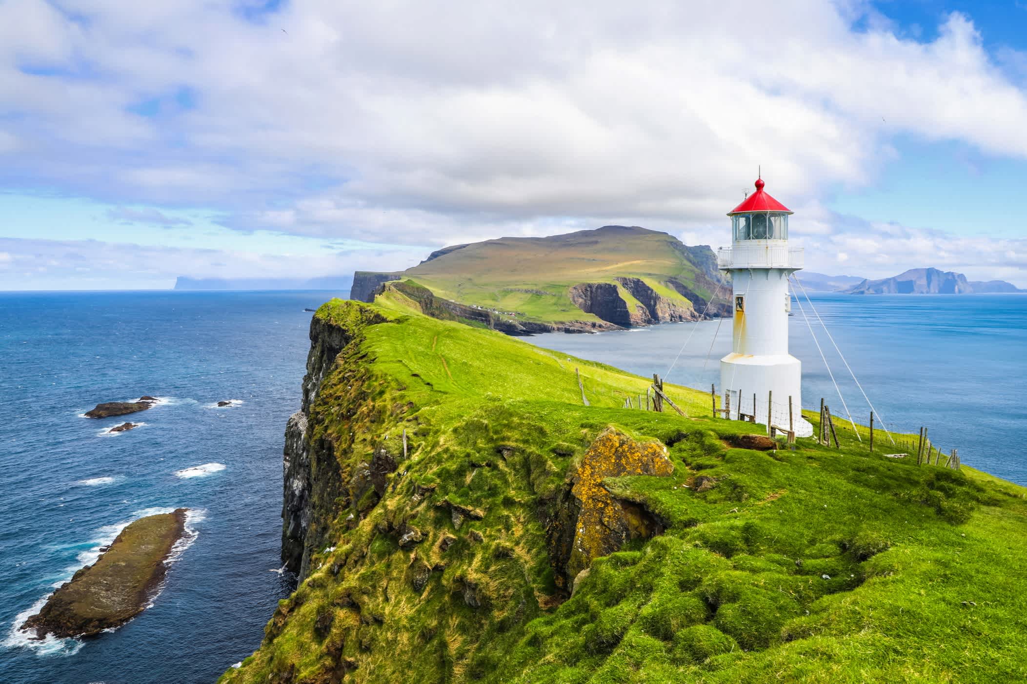 Vue sur un phare et un paysage de collines verdoyantes avec la mer en arrière-plan