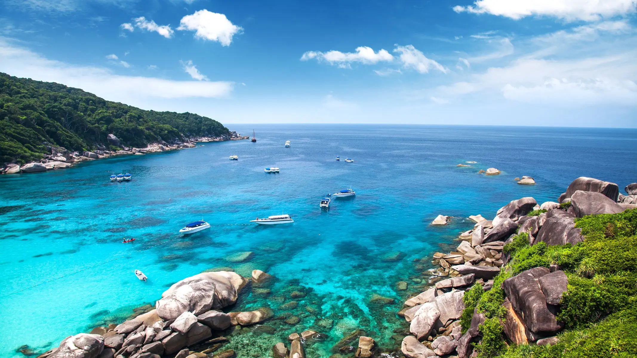 Boote im Wasser einer Bucht umgeben von üppiger Vegetation und Felsen, Similan Inseln, Thailand. 