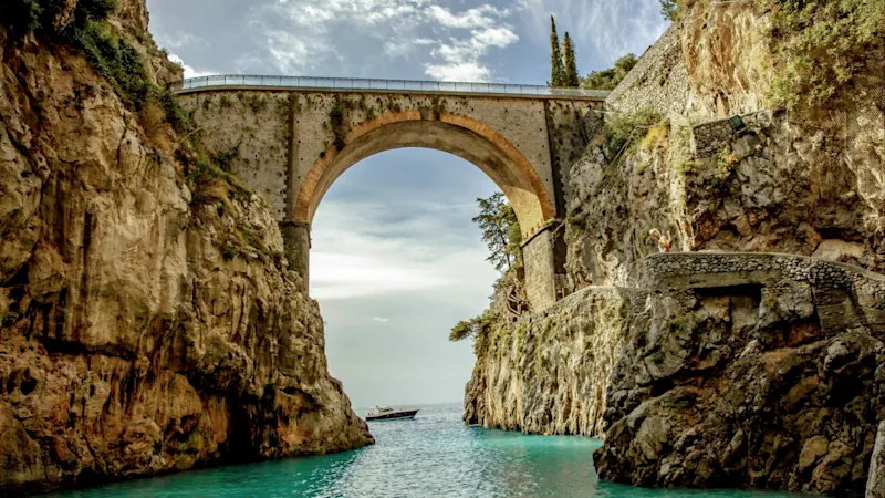 View of an old stone bridge in a small bay between large rocks and the sea below