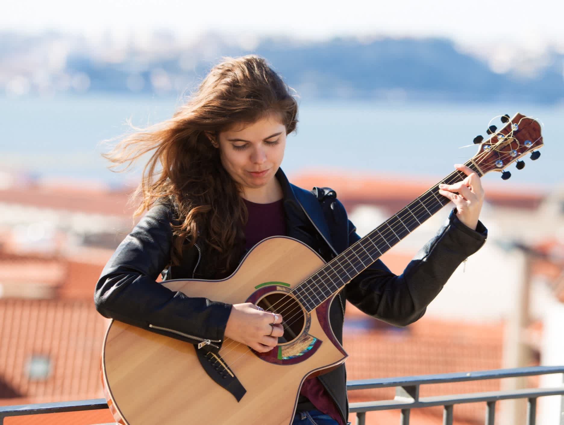 Ein Mädchen spielt Gitarre über den Dächern Lissabons, Portugal. 