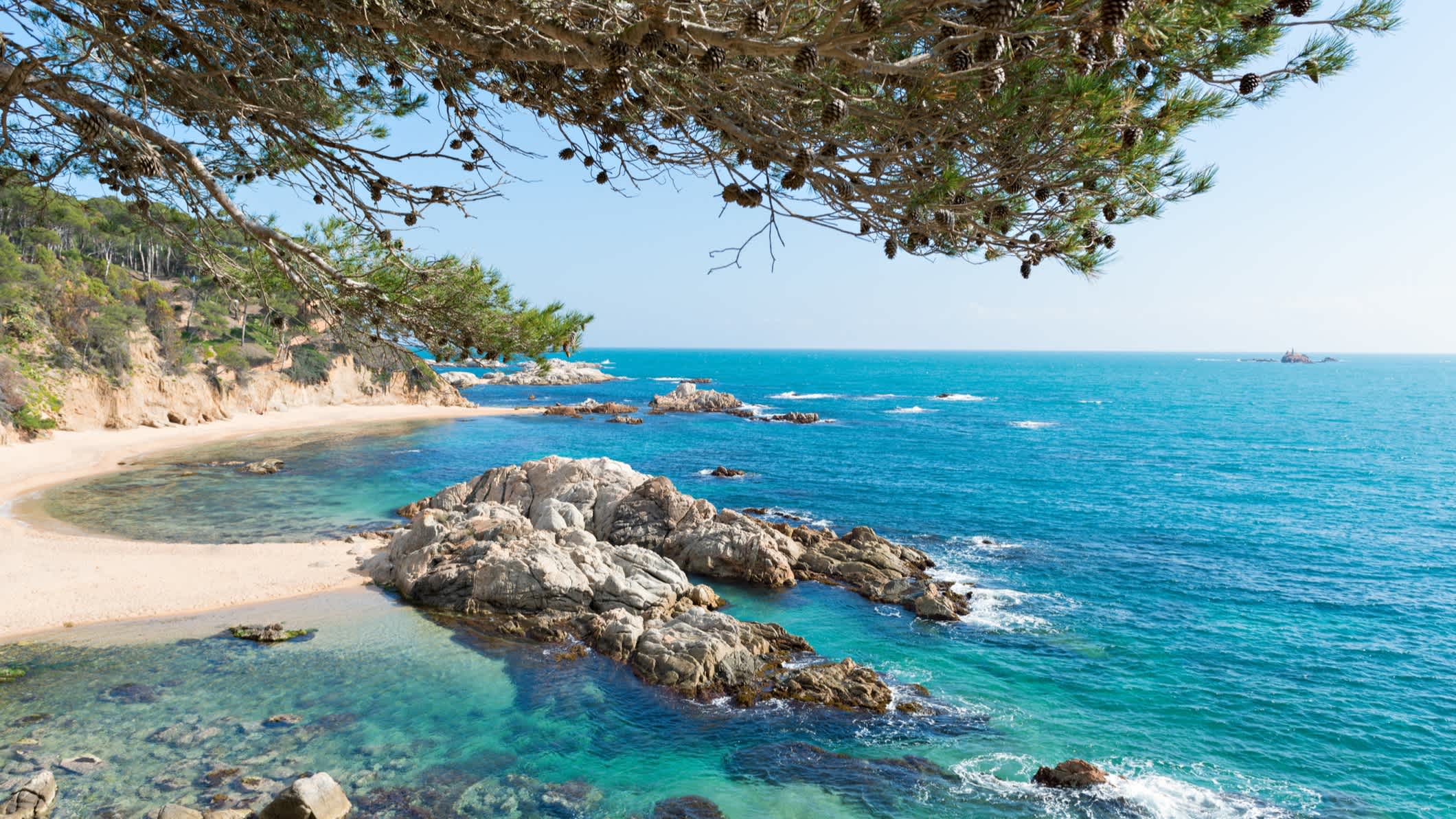 Rocher dans l'eau turquoise au bord du sable blanc entouré de falaise sur la plage de Sant Pere Pescador en Espagne. 