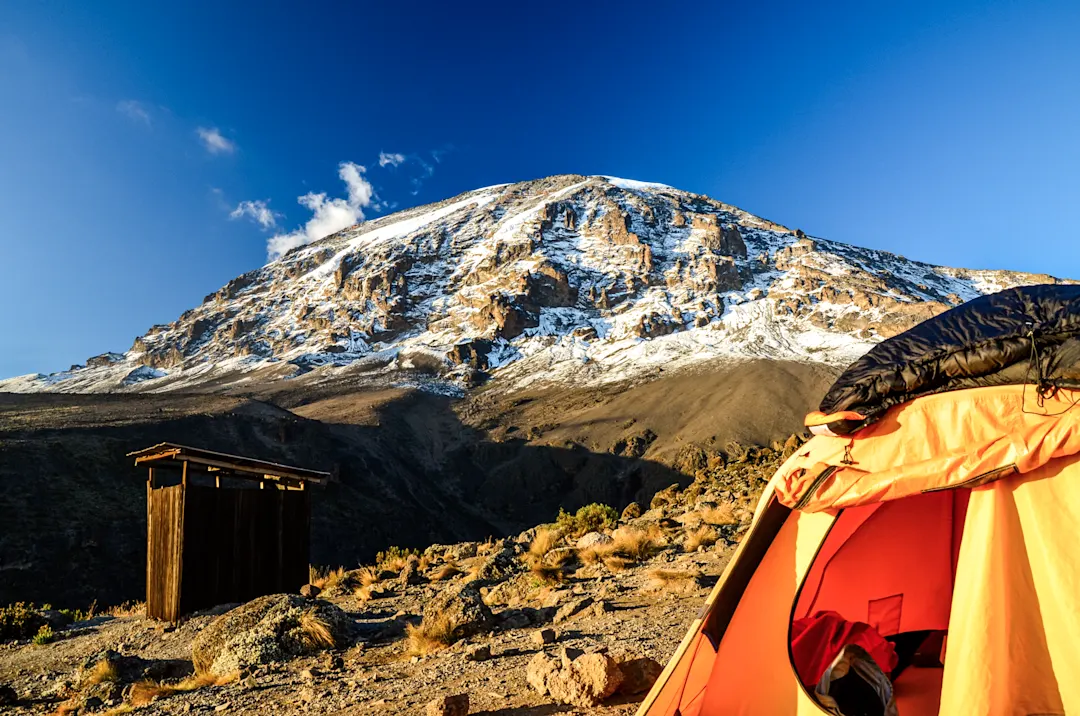 Nahaufnahme eines orangefarbenen Zeltes mit dem schneebedeckten Berg im Hintergrund, Kilimandscharo, Tansania