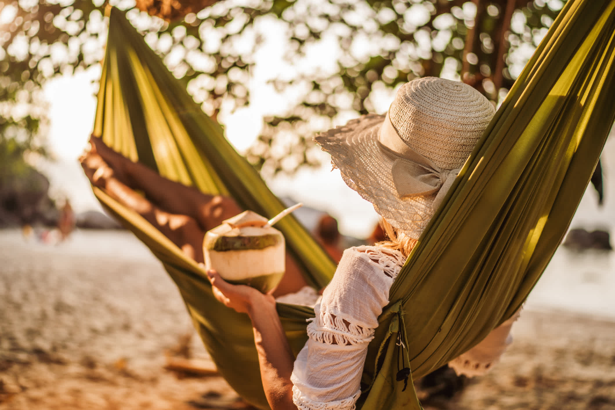 Die Frau mit Kokosnuss-Drink entspannt sich in der Hängematte am Strand.

