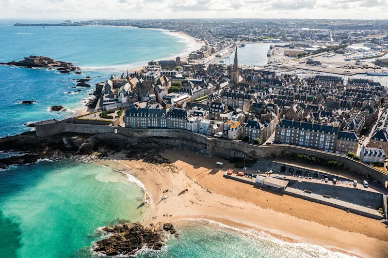 Aerial view of Saint-Malo, France with historic walled city, sandy beaches, and turquoise waters along the coastline.