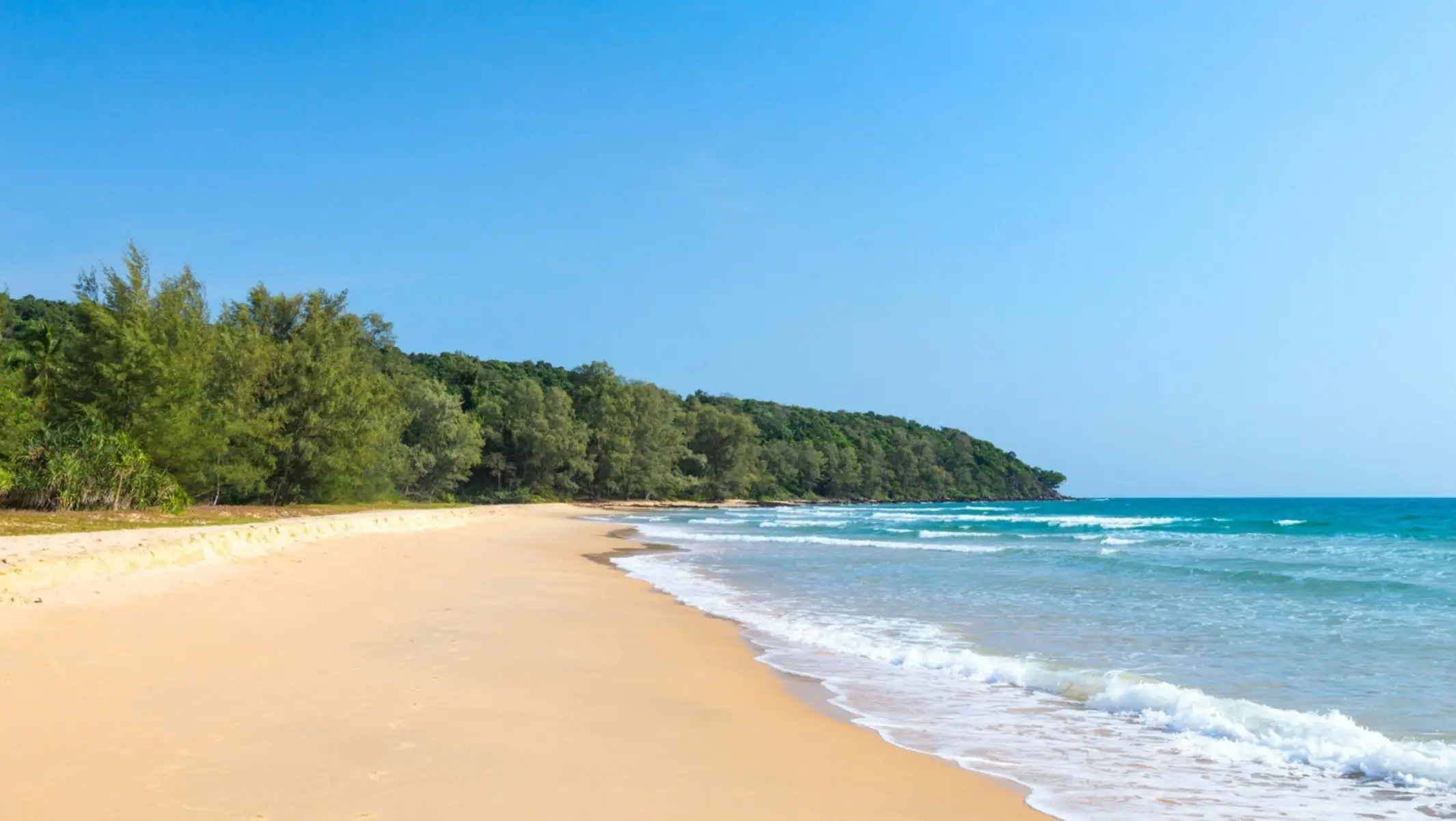 Gelber, langer Sandstrand am Meer des Lonely Beach, Cambodia mit natürlicher Vegetation am Rand sowie Sonnenschein.