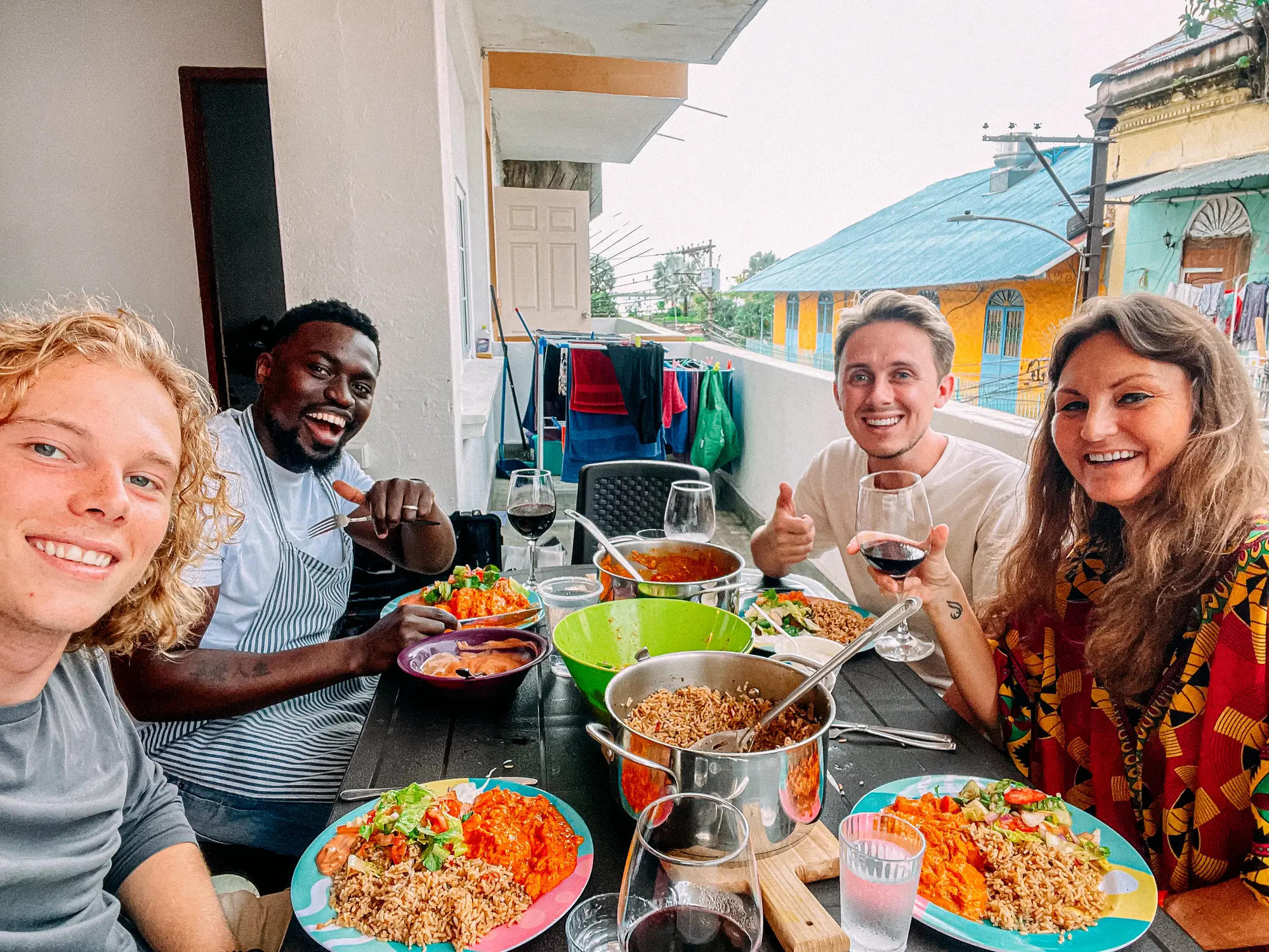 Panama-City, Food Neue Freundschaften! Selfie einer lächelnden multiethnischen Gruppe von Freunden Teilen Sie ein köstliches Erdnuss-Curry-Hühnergericht, Salat, gewürzten Reis und Rotwein für eine lokale Dinnerparty Food Tour-Erlebnis auf einem Balkon in Panama City, Panama