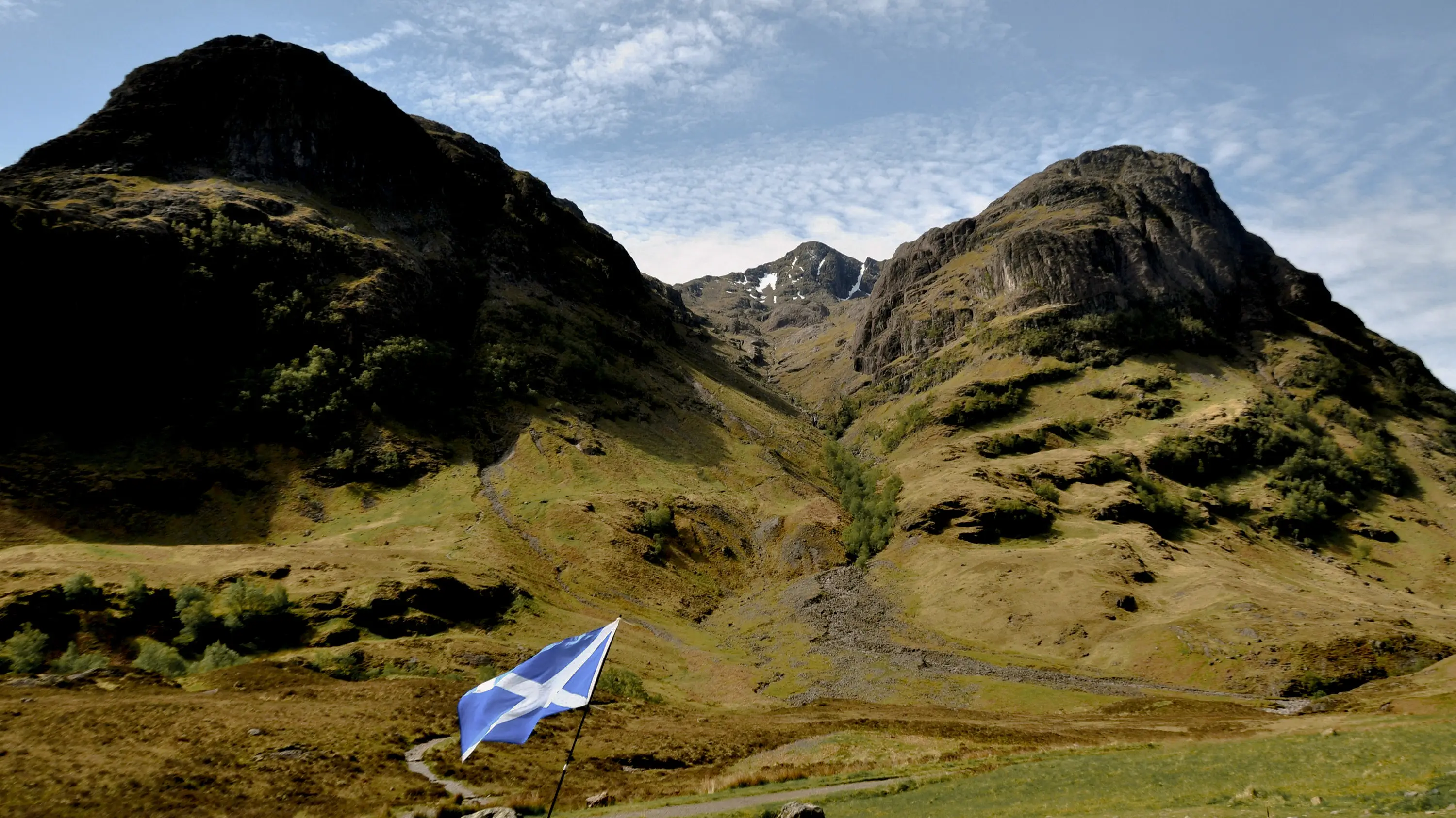 A Three Sisters mountain range in Glencoe with a Scottish flag in the foreground, Scotland