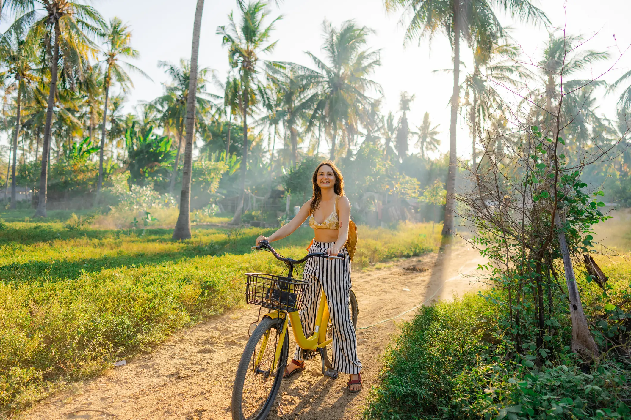 Indonésie, tour à vélo Une femme joyeuse fait du vélo dans une cocoteraie en Indonésie.