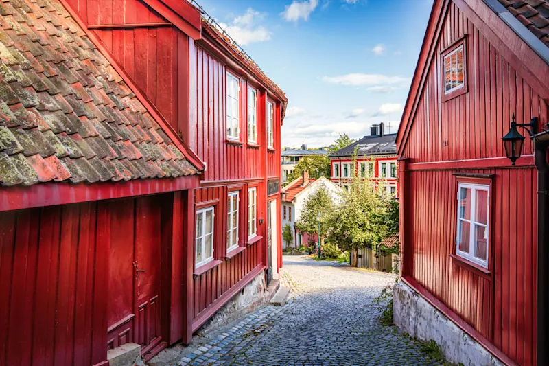 Rue vieille ville Oslo Norvege Ruelle pavée entre maisons traditionnelles rouges scandinaves sous un ciel bleu, menant vers un quartier résidentiel ensoleillé à Oslo, Norvège