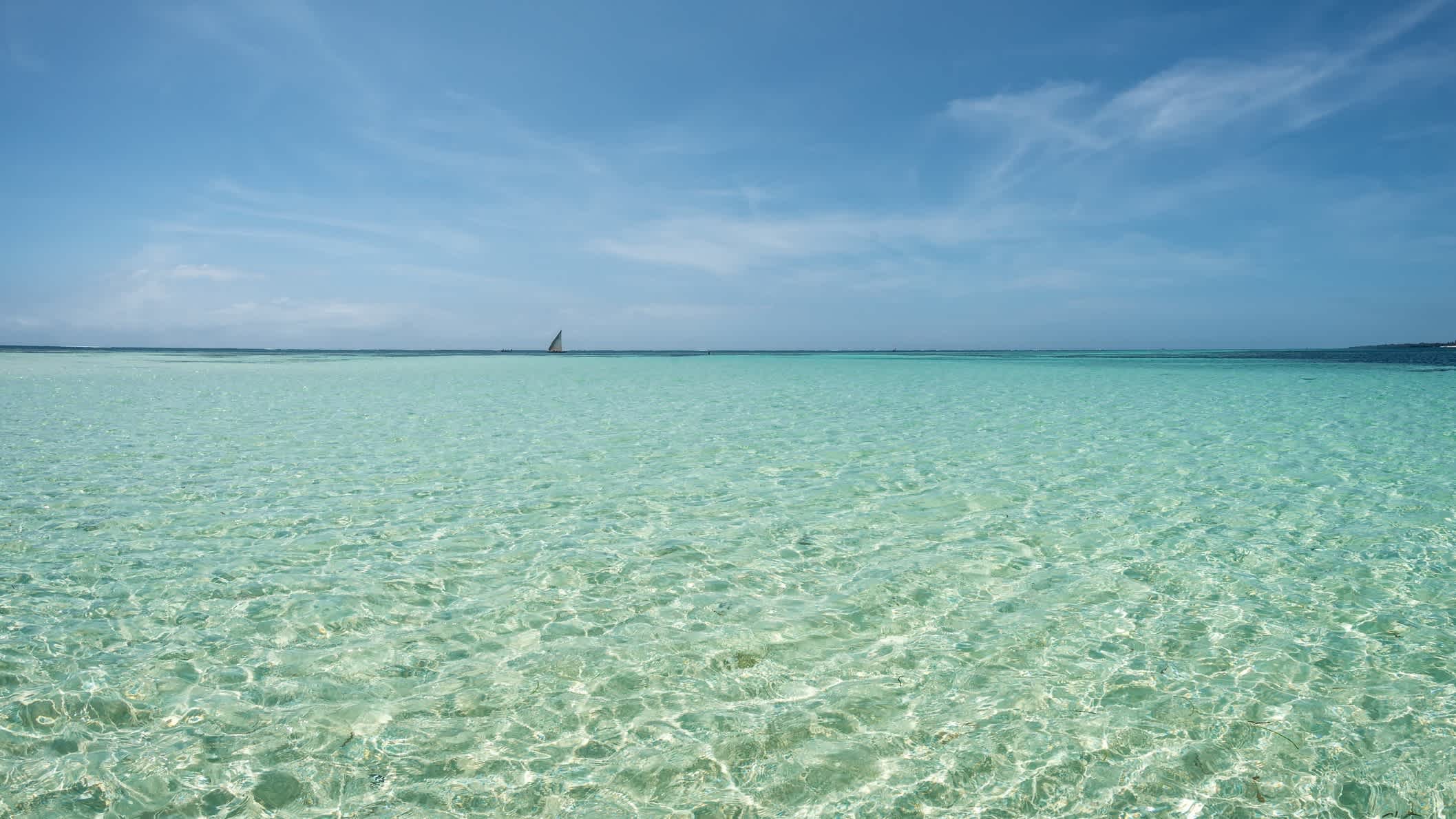 Kristallklares Wasser am Che Shale Beach in Kenia bei purem Sonnenschein und mit einem Segelboot am Horizont. 