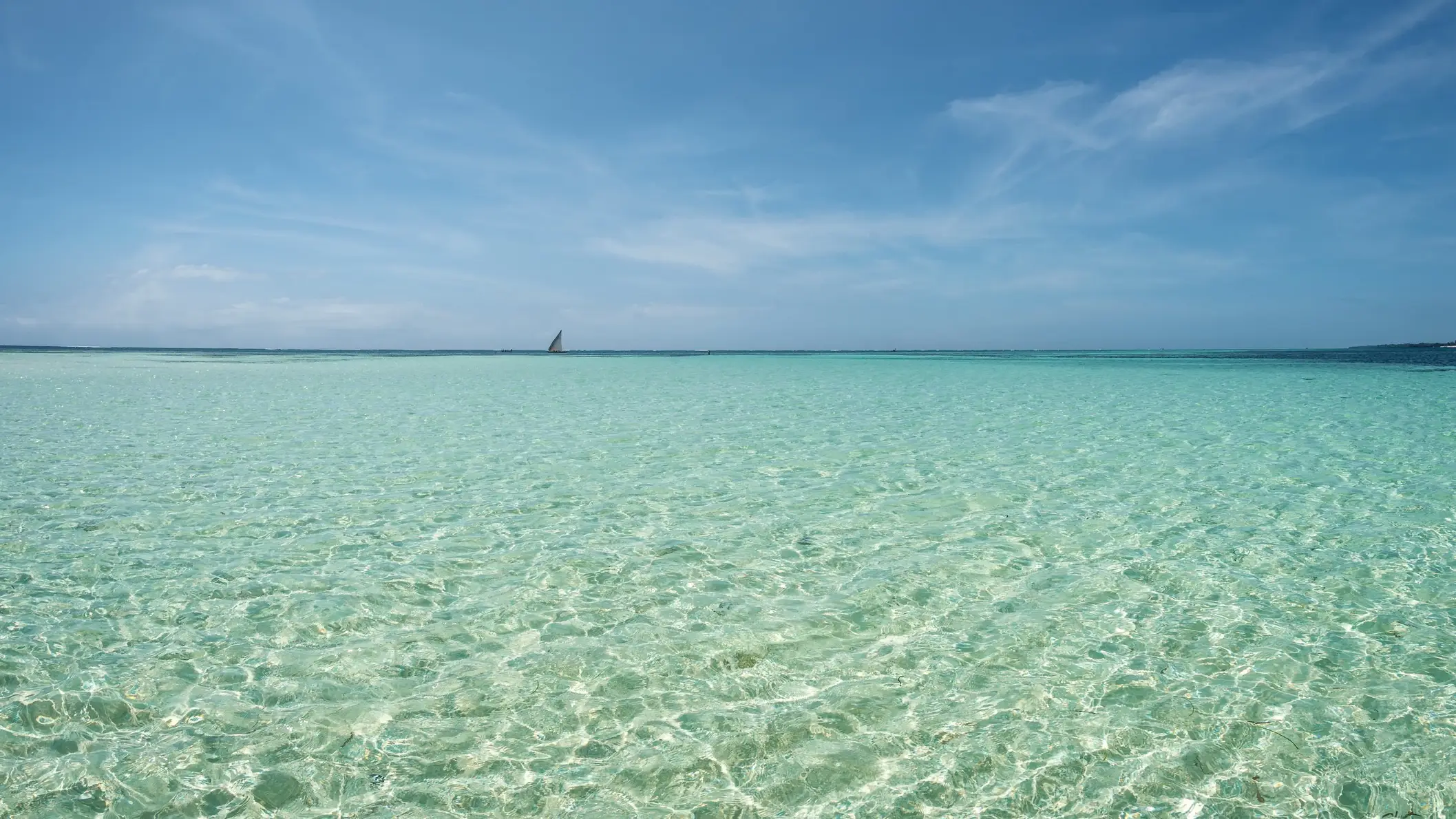 Kenia Che Shale Beach Kristallklares Wasser am Che Shale Beach in Kenia bei purem Sonnenschein und mit einem Segelboot am Horizont.