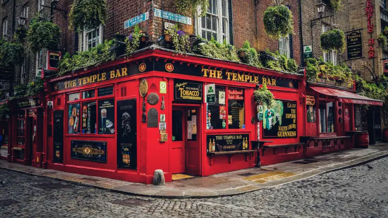 Le Temple Bar, pub irlandais emblématique à façade rouge vif, décoré de plantes et situé sur une rue pavée à Dublin.