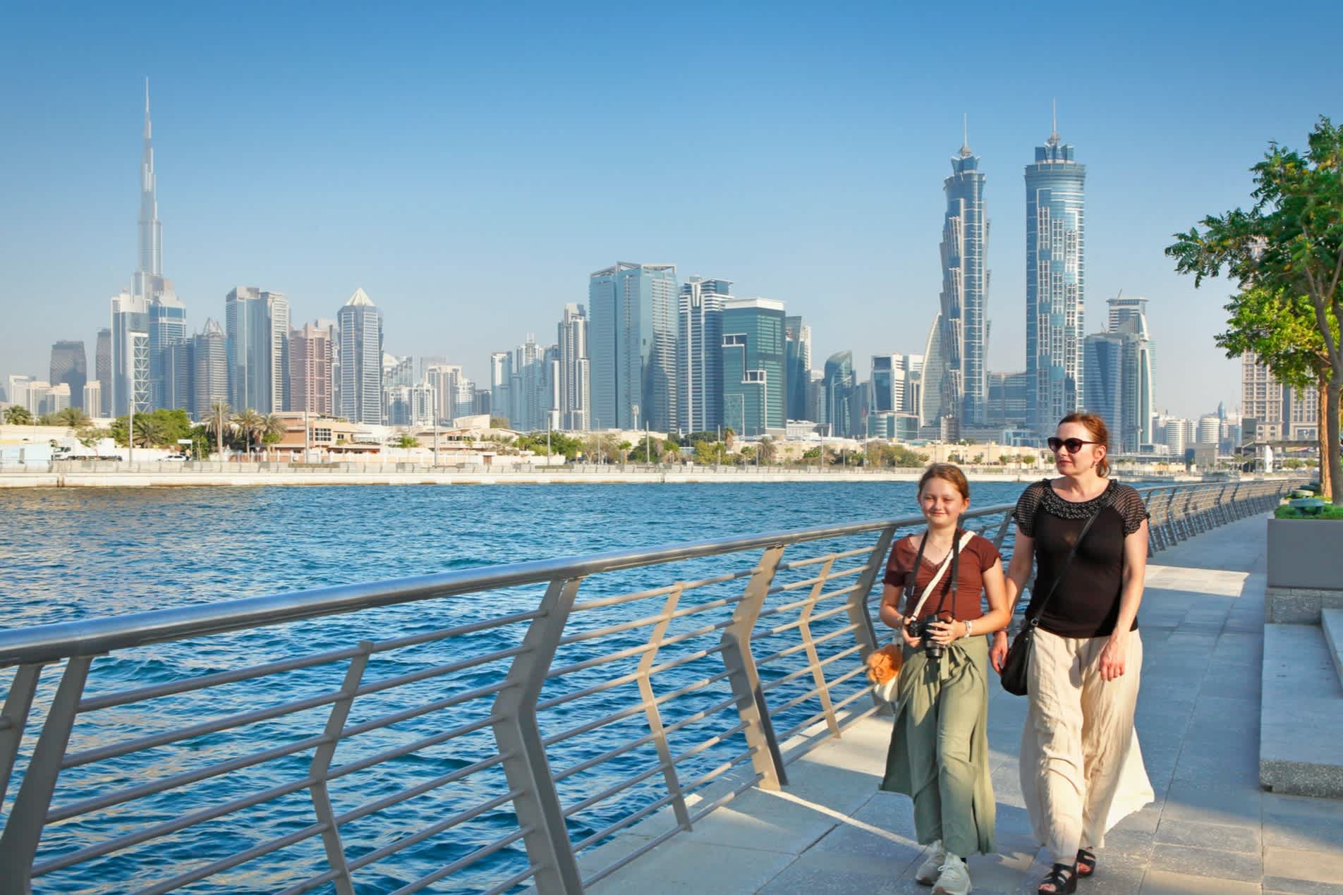 Mutter und Tochter spazieren am Kanal in Dubai entlang mit der Skyline im Hintergrund
