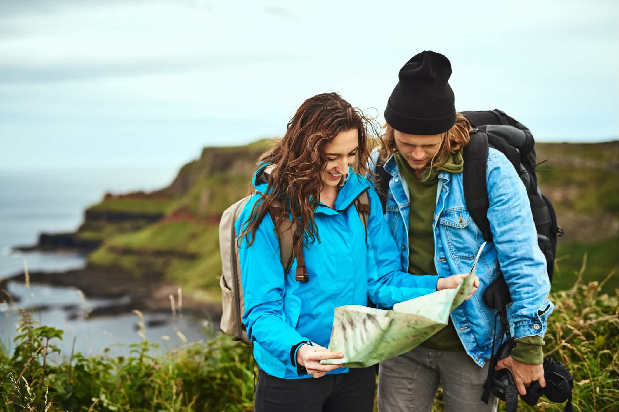 Ein junges Paar sucht auf einer Landkarte nach dem Weg im Freien, Irland. 