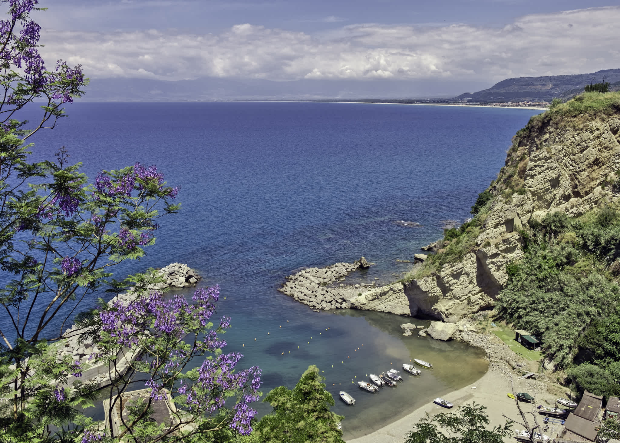 Luftaufnahme einer Strandbucht in Kalabrien, umgeben von Felsen und üppiger Vegetation.