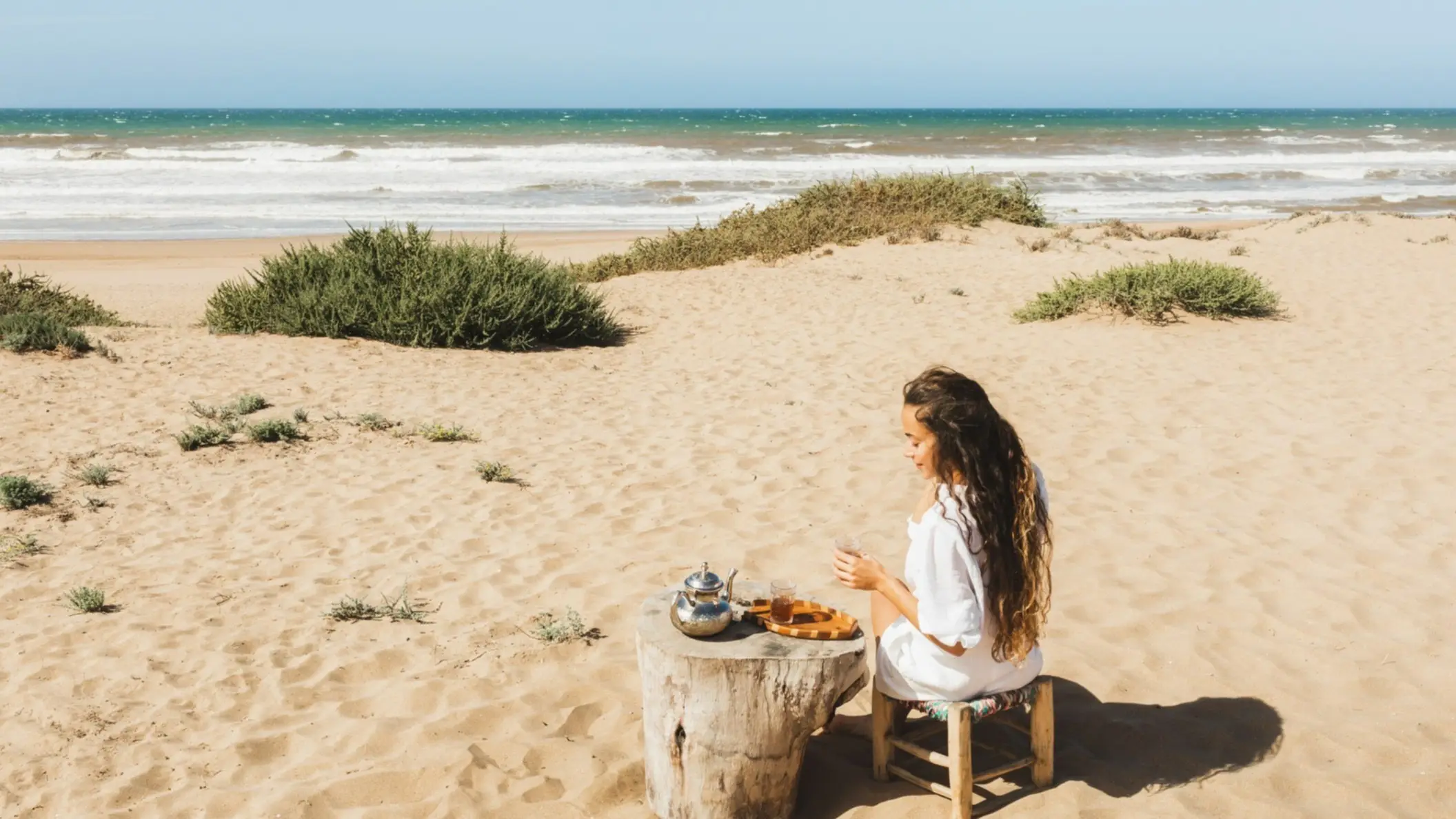 Marokko Frau genießt marokkanischen Tee am Sandstrand des Kaf Lahmam, Tanger-Tétouan-Al Hoceïma, in Marokko bei sonnigem Wetter.