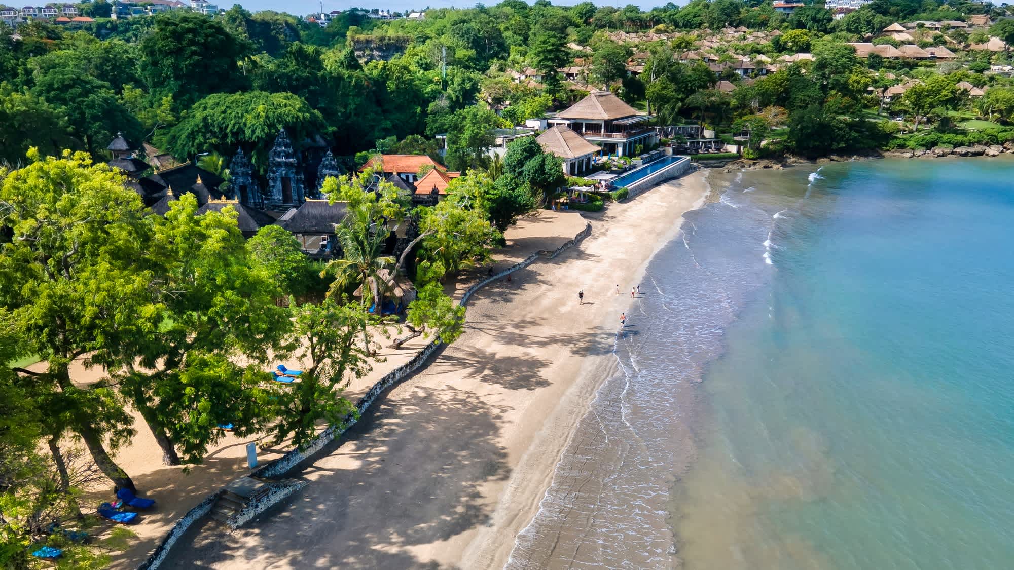 Luftaufnahme des Jimbaran Beach auf Bali, Indonesien mit grüner Vegetation im Bild und Häusern am Strand.