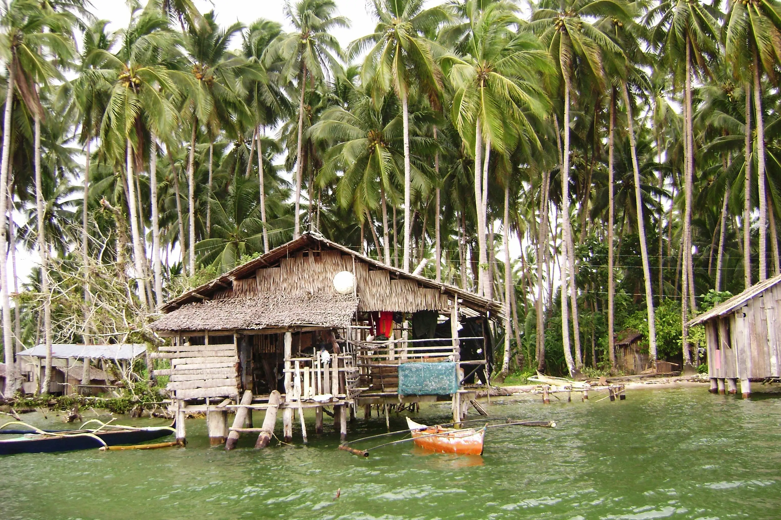 Mittelweite Aufnahme eines Hauses auf Stelzen mit Booten vor einem Fischerdorf in Surigao del Sur, Philippinen.


