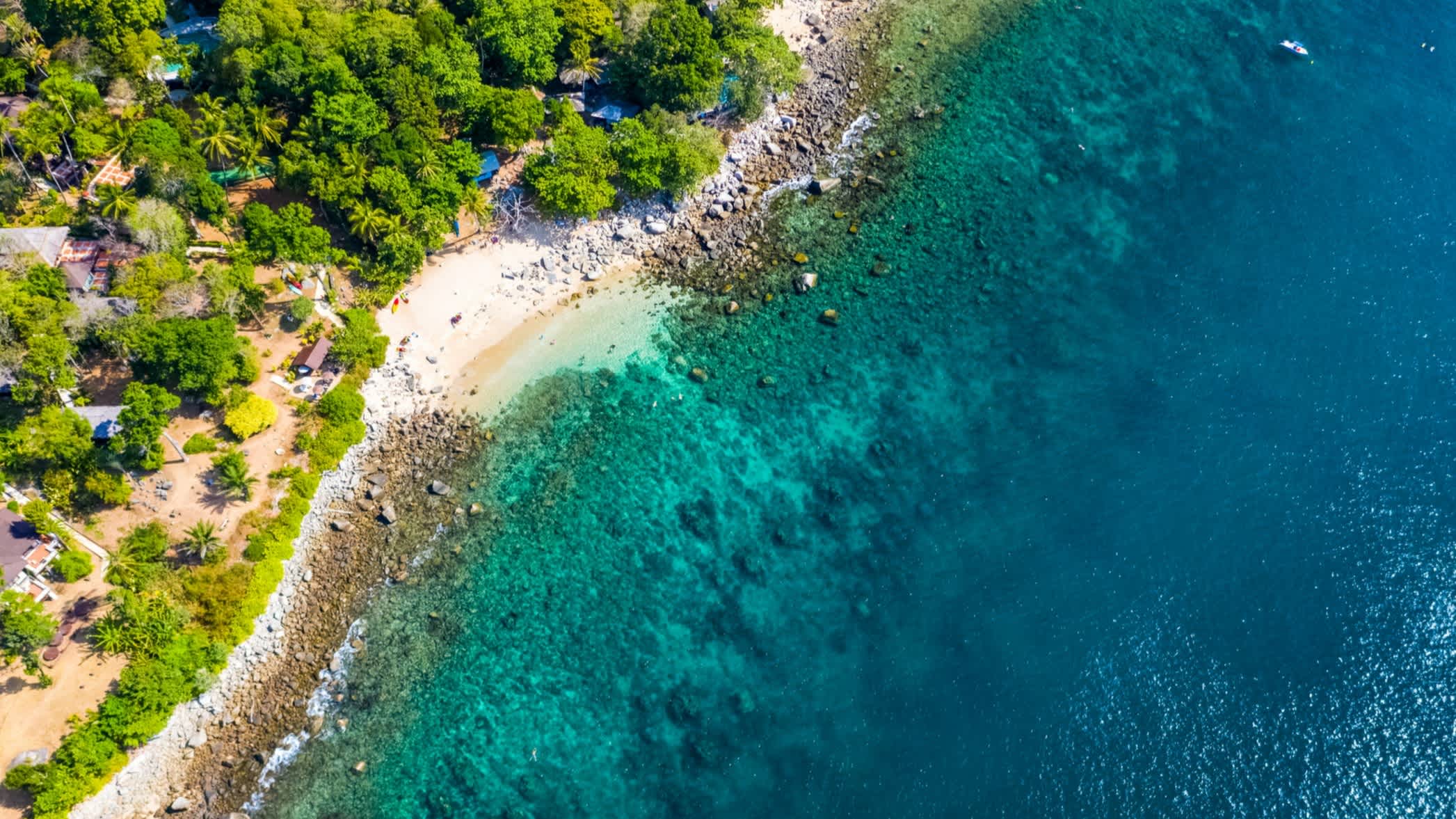 Luftaufnahme des Ao Sane Beach auf Phuket, mit cyanblauem Wasser, Felsenküste und üppig grüner Vegetation.