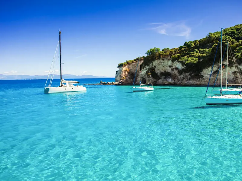 Grèce, Corfou, Kassiopi Voiliers sur une eau claire et bleue avec falaises verdoyantes. Kassiopi, Corfou, Grèce.