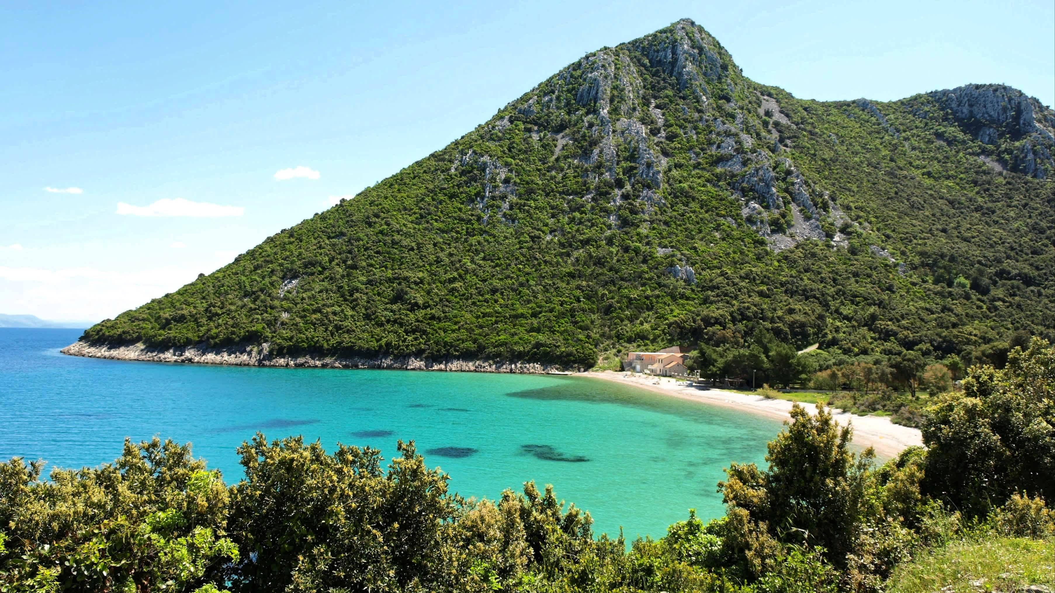 Der Strand von Divna, Halbinsel Pelješac, Kroatien mit Blick auf einen hohen Berg und das türkise Wasser.