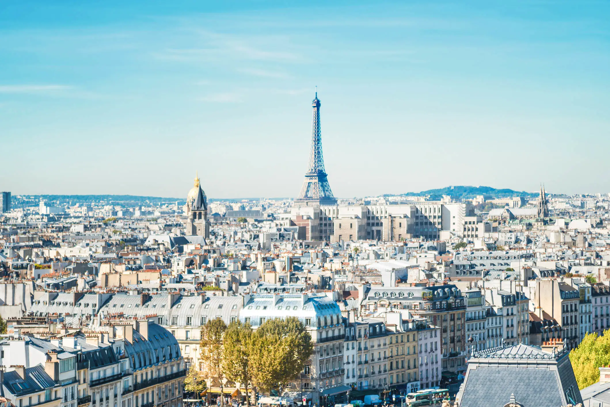 Panoramic view of Paris skyline with the Eiffel Tower rising above historic buildings under a clear blue sky.