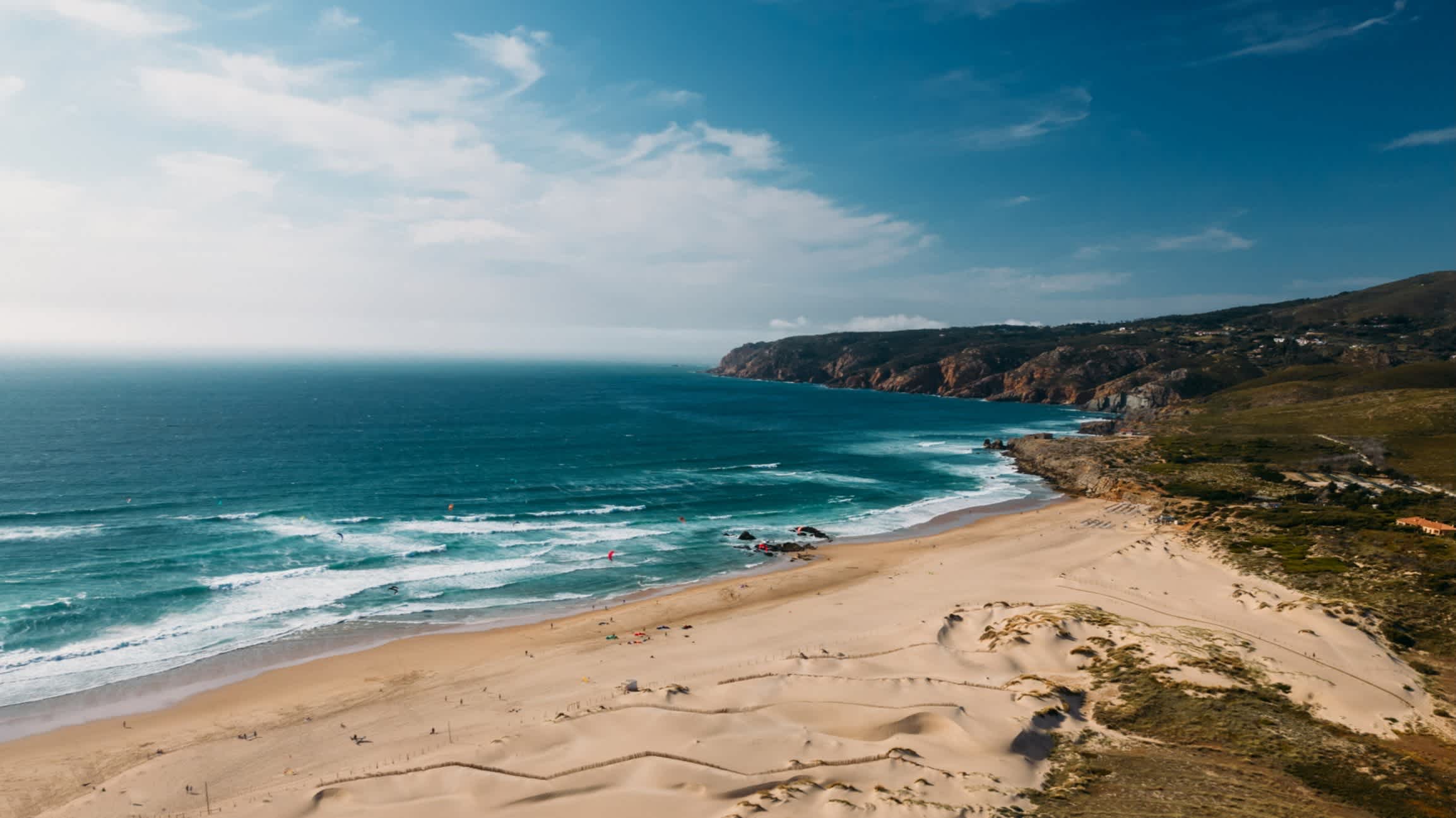 Naturbelassener Strand von Praia do Guincho, Cascais, Portugal mit wolkenfreiem Himmel und Blick auf das weite Meer.