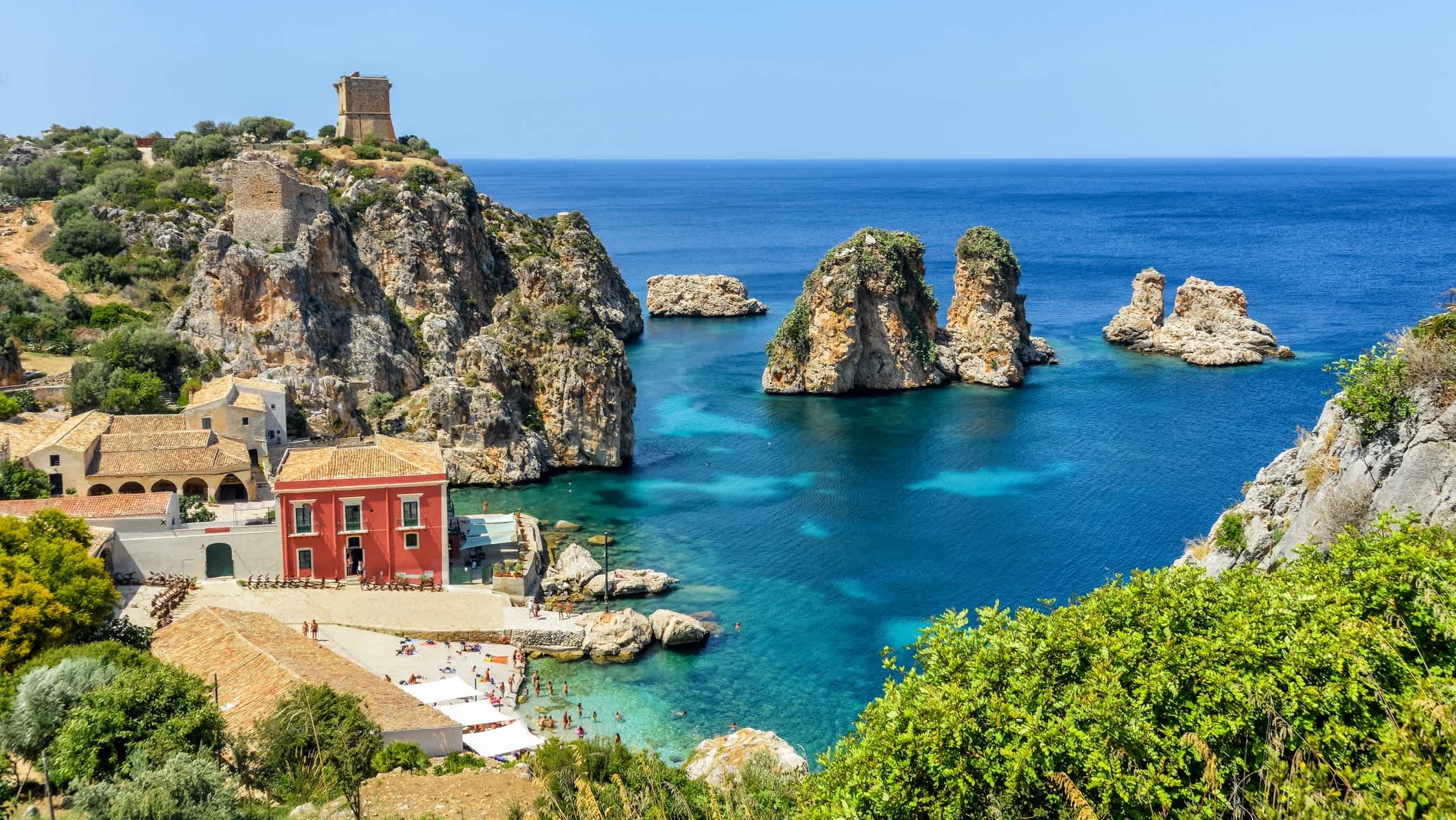 Schöner Strand von Scopello in Sizilien, Italien mit einem roten Haus und natürlicher Vegetation im Bild.
