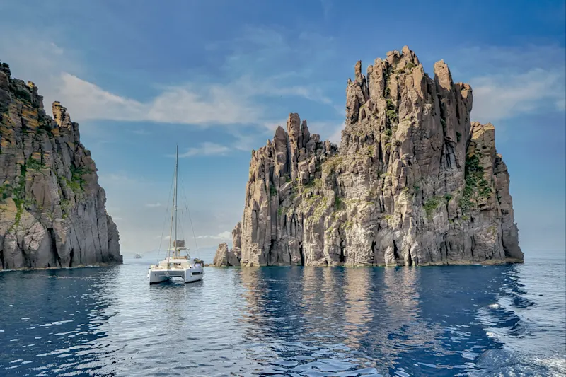 Sailing boat between rocks in blue water. Lipari, Sicily, Italy.
