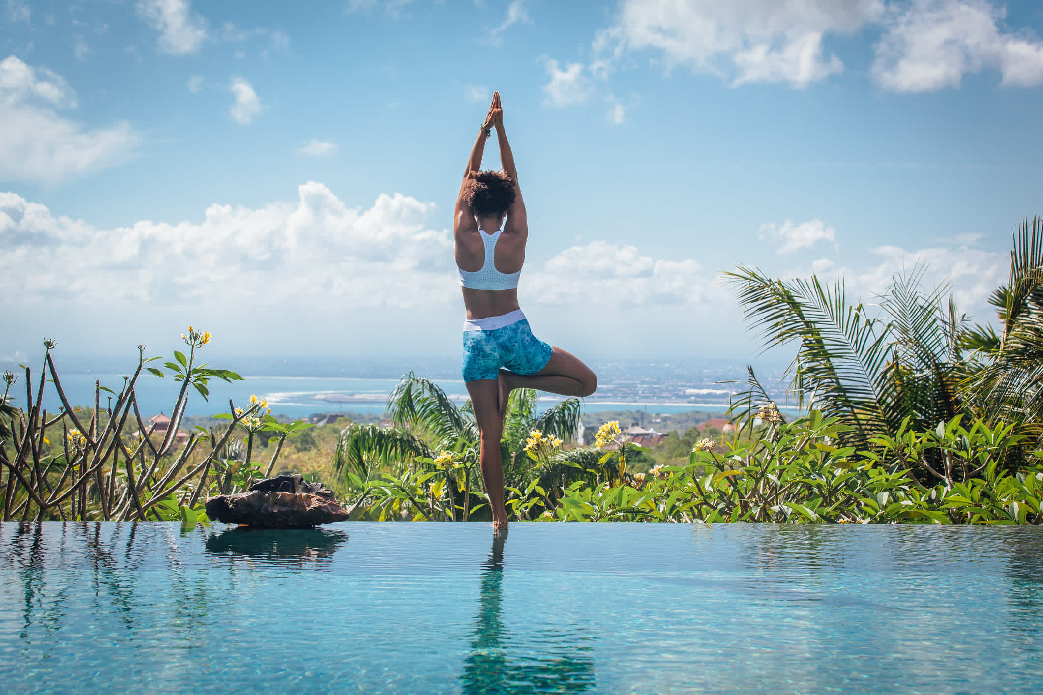 Eine Frau praktiziert Yoga am Rande des Infinity-Pools in Bali, Indonesien.

