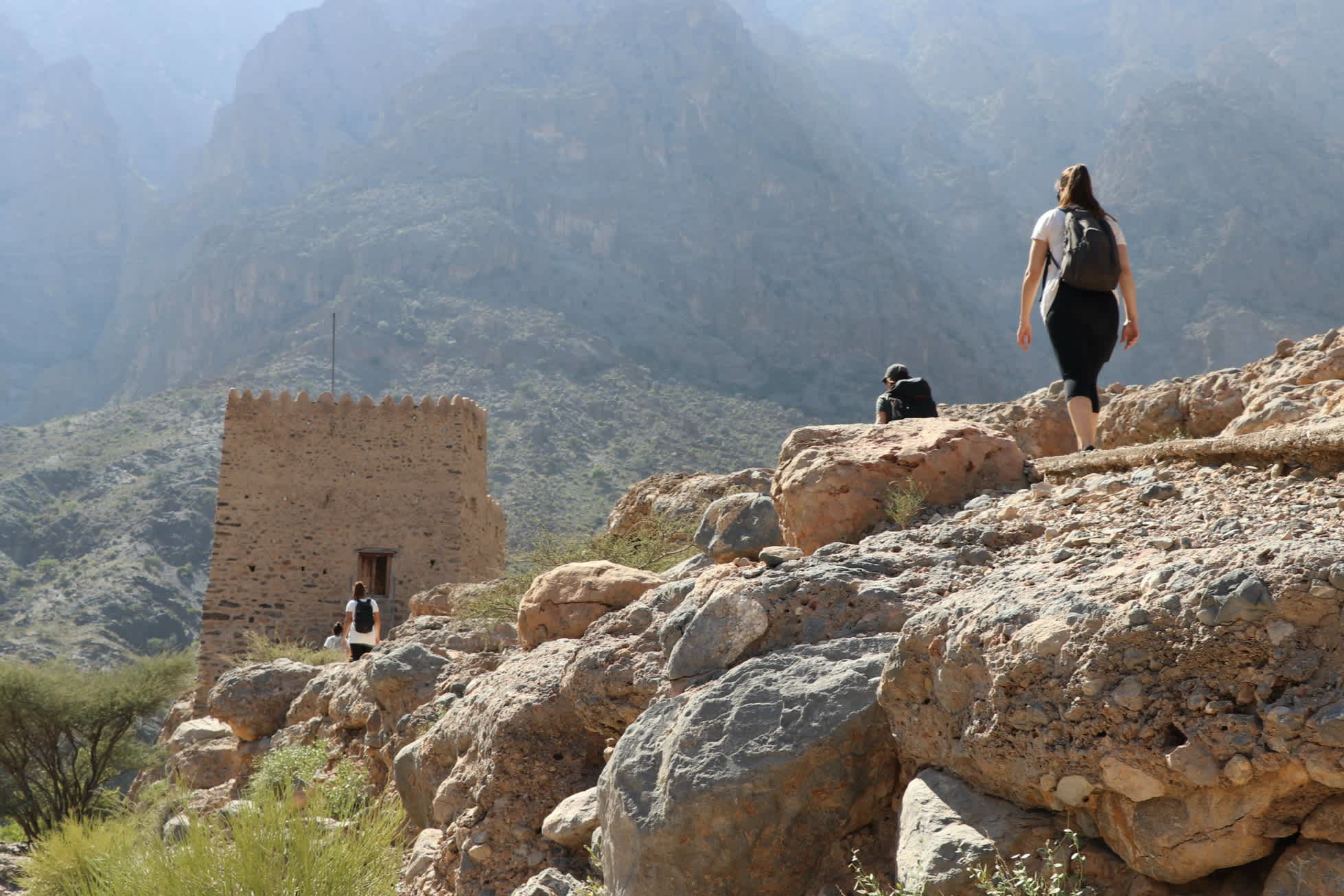 Drei Menschen wandern durch eine Berglandschaft im Oman