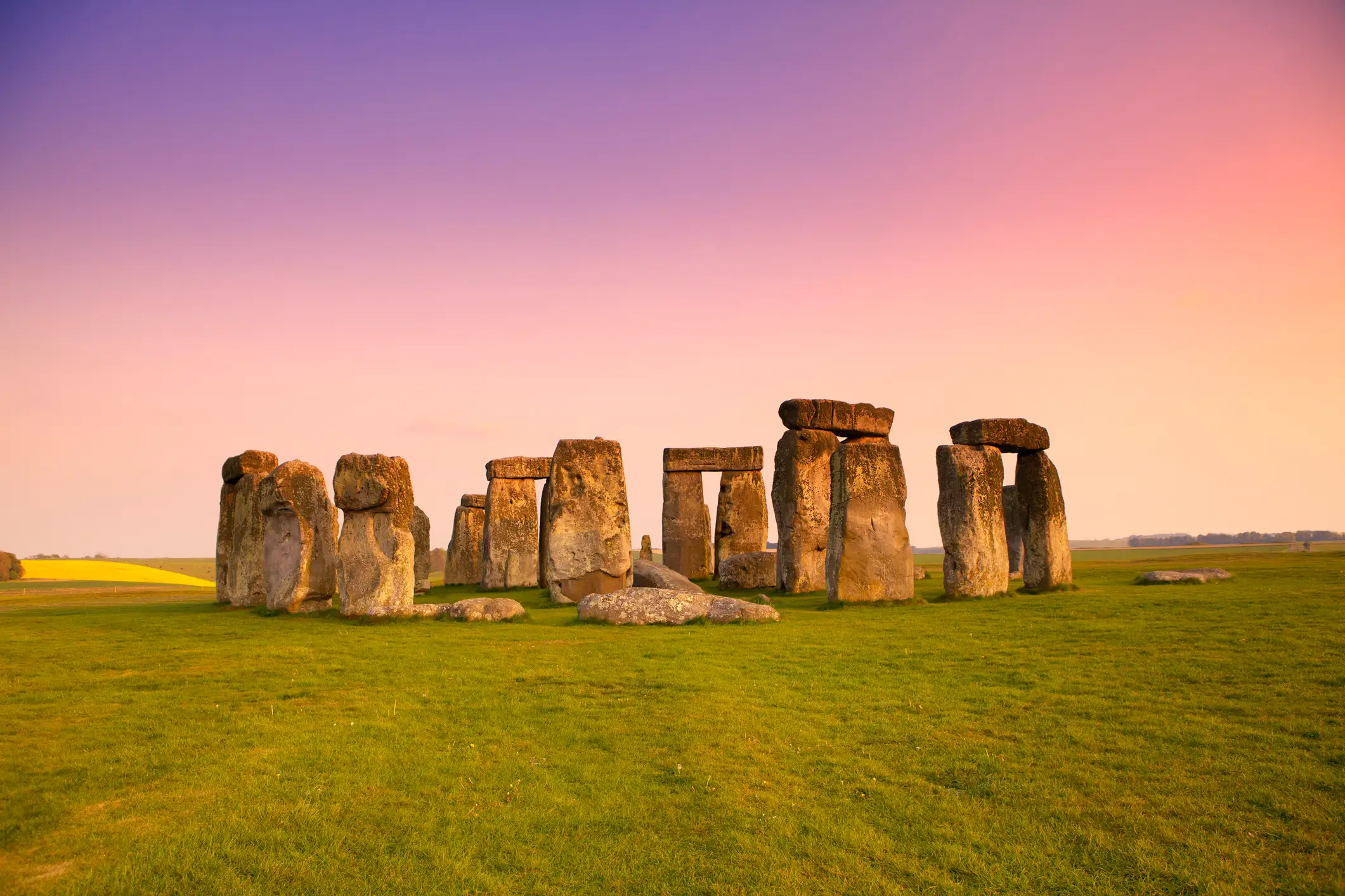 Alter Steinkreis von Stonehenge auf einer Wiese unter einem farbenprächtigen Sonnenuntergangshimmel, mit großen aufrecht stehenden Steinen, die in einer Kreisformation angeordnet sind.