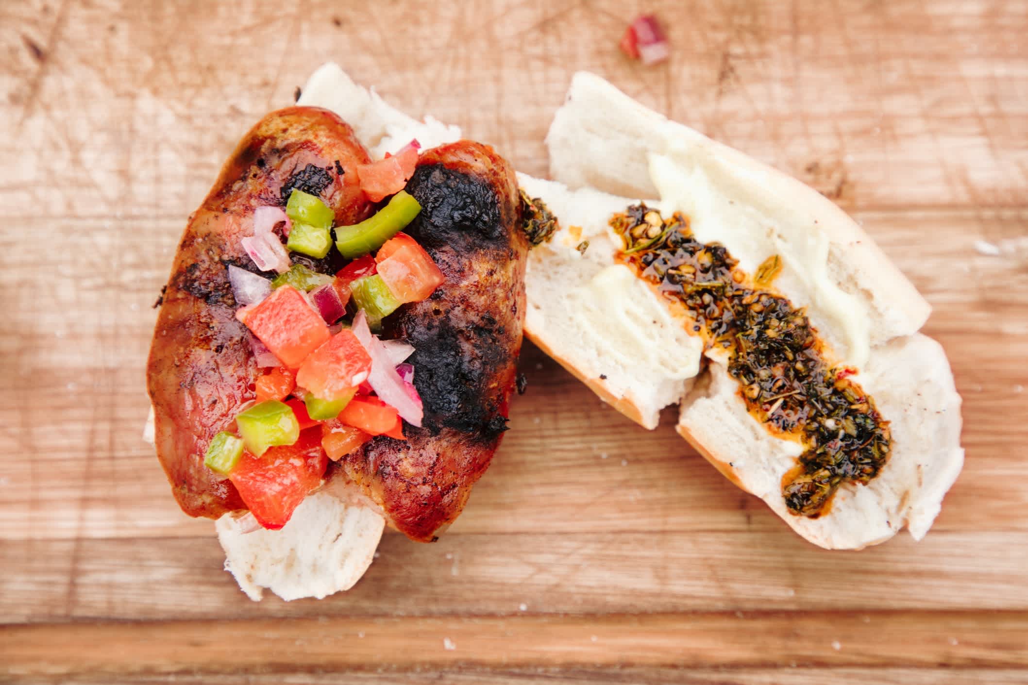 De haut en bas, vous voyez le sandwich argentin Choripan Hot Dog sur une planche à découper, assaisonné de salsa à la tomate et à l'oignon, de mayonnaise et de chimichurri.