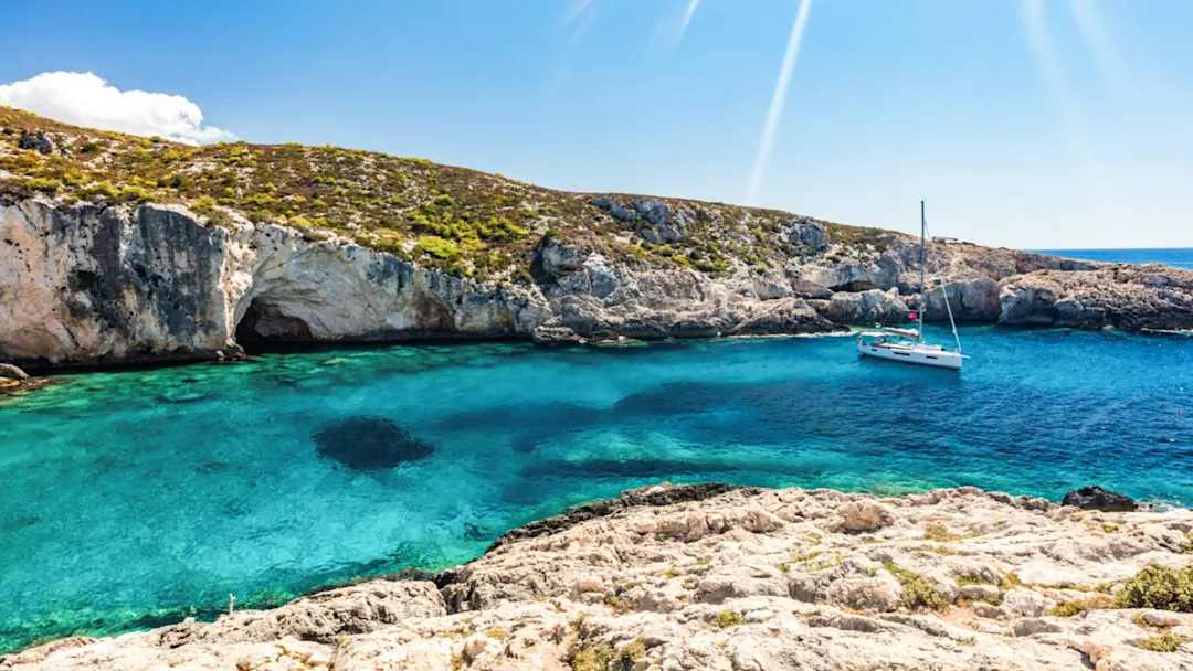 Segelboot im türkisfarbenen Wasser vor Felsen und Höhle, Limnionas, Zakynthos, Griechenland.