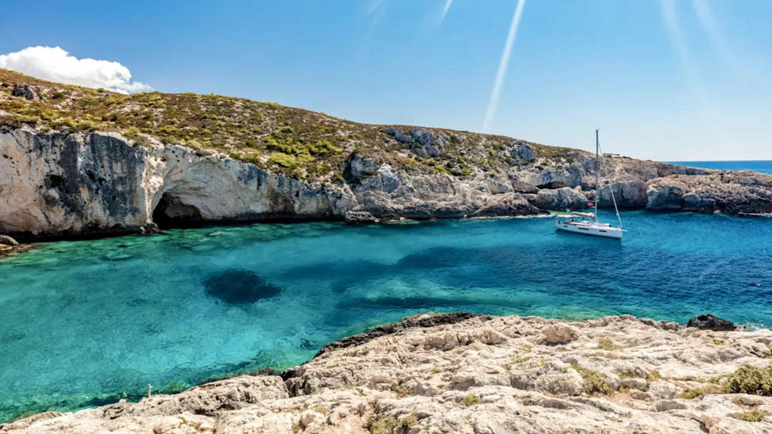Segelboot im türkisfarbenen Wasser vor Felsen und Höhle, Limnionas, Zakynthos, Griechenland.