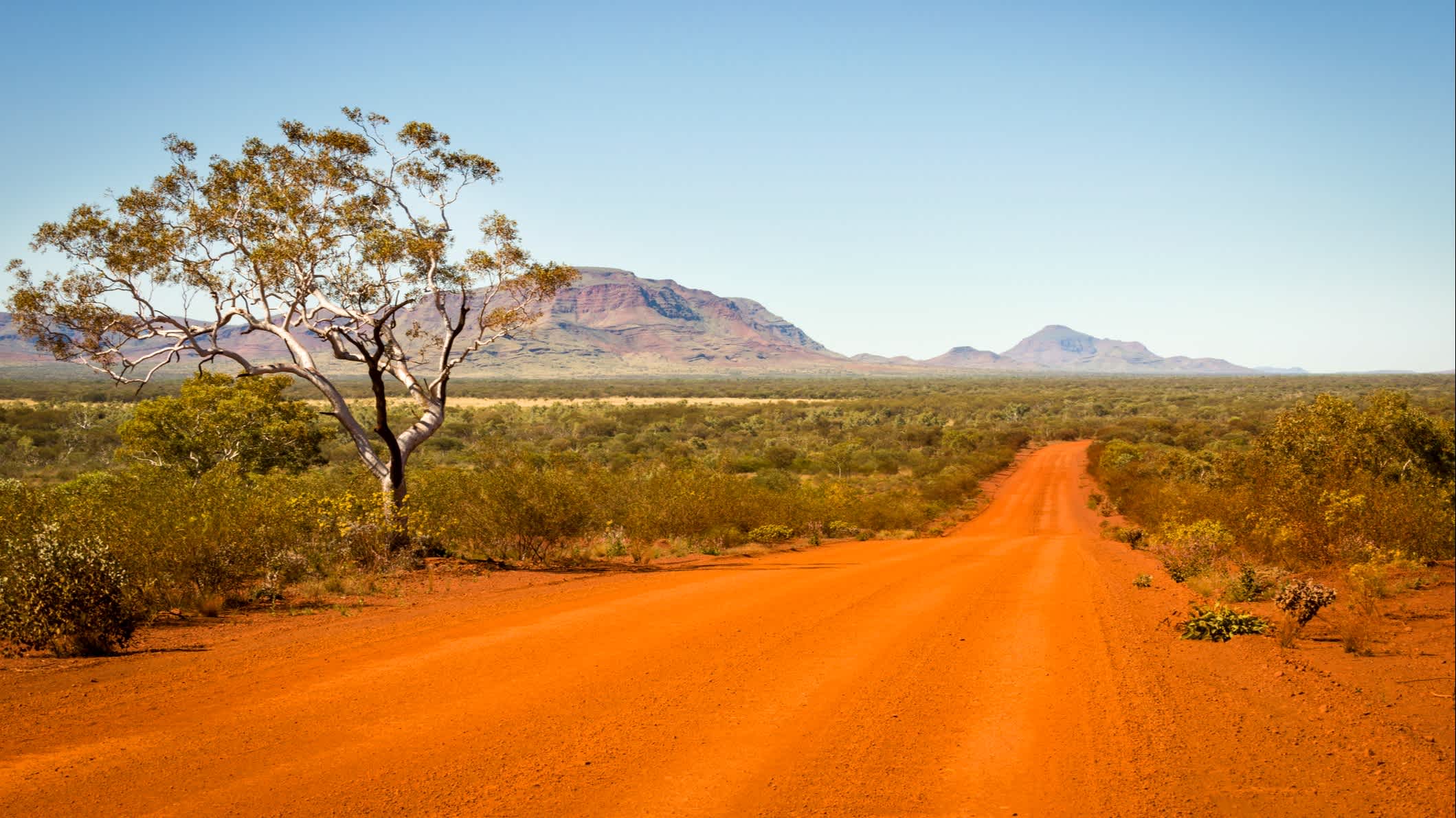 Route rouge avec une chaîne de montagnes en arrière-plan, Outback, Australie.