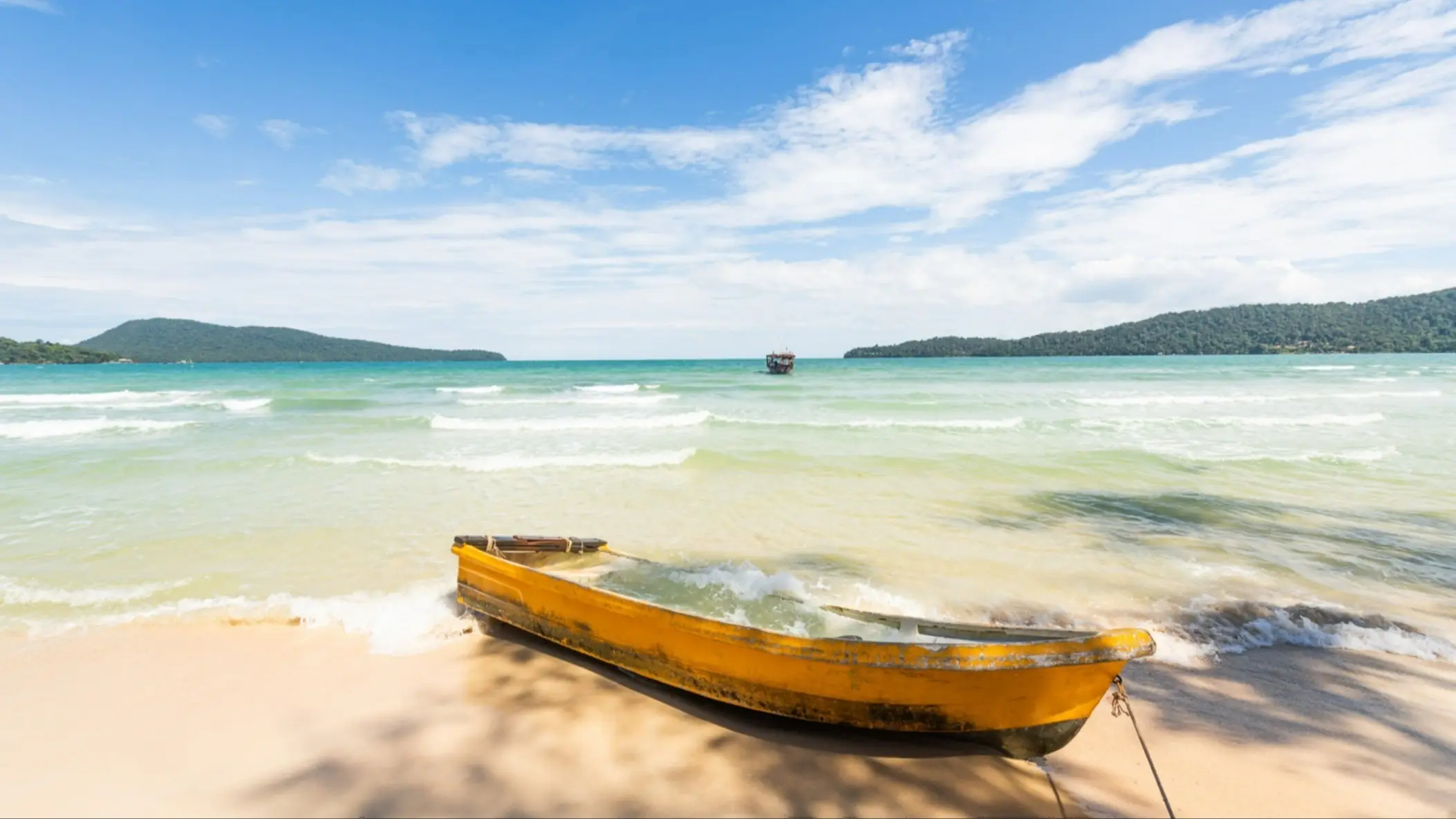 Koh Tonsay, Kambodscha Gelbes Boot am Strand von Koh Tonsay, Kambodscha bei seichten Wellen und blauem Himmel.