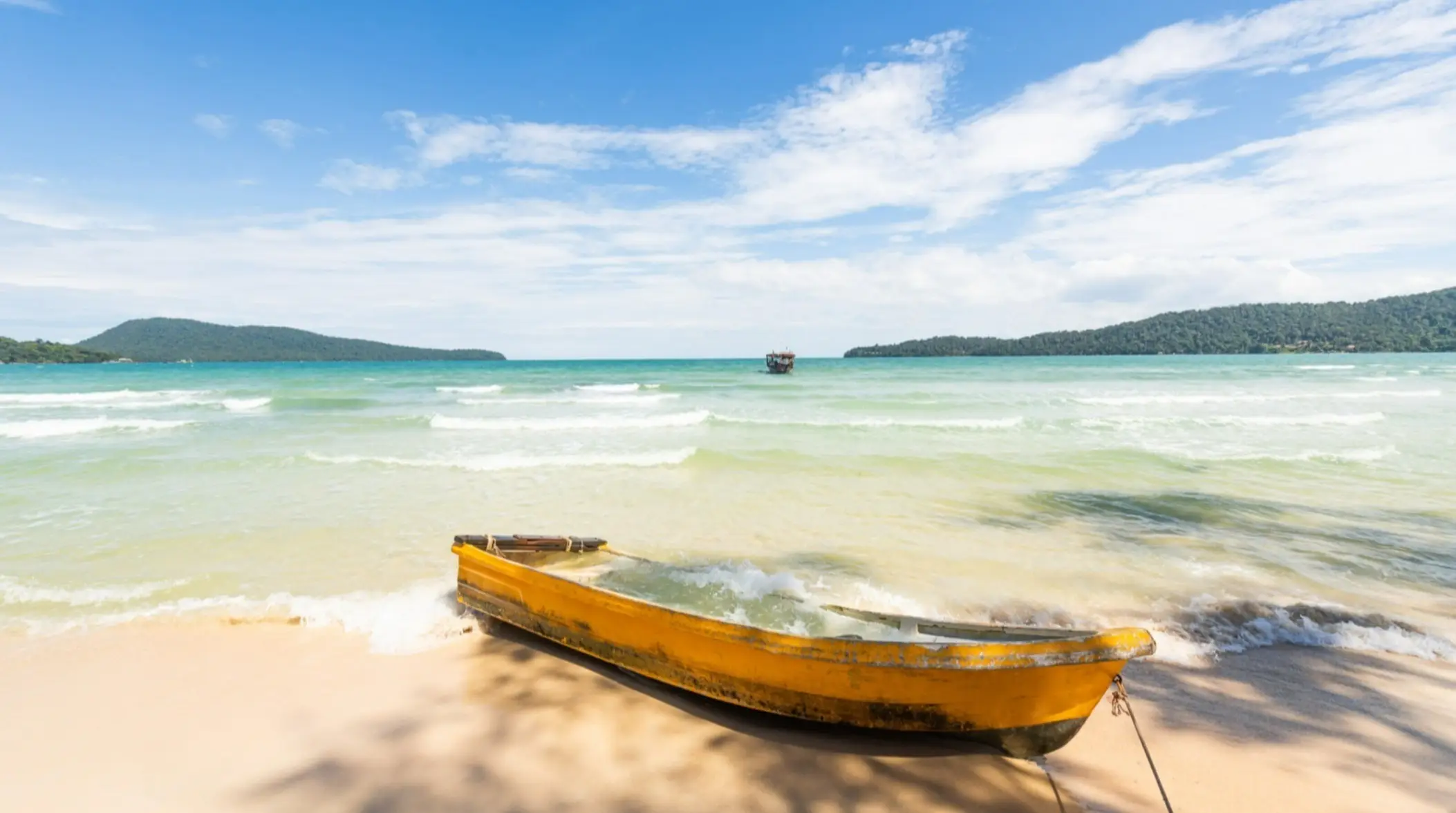 Gelbes Boot am Strand von Koh Tonsay, Kambodscha bei seichten Wellen und blauem Himmel.