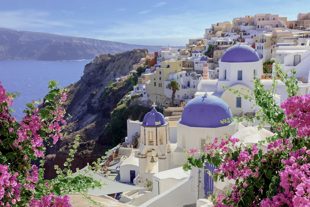 Weiße Häuser mit blauen Kuppeln und Blumen auf Klippe, Oia, Santorini, Griechenland