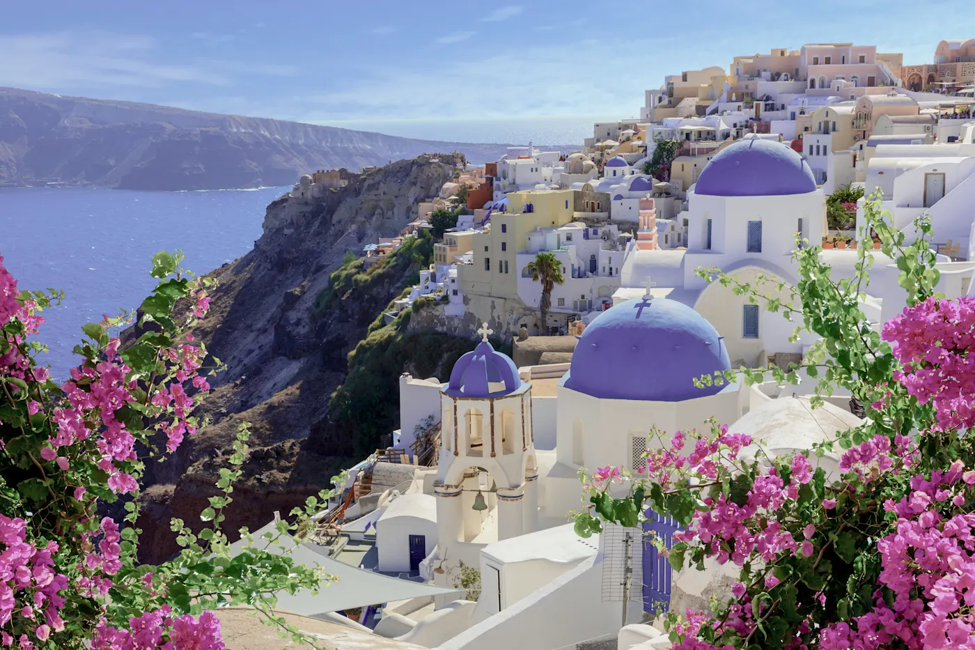 White houses with blue domes and flowers on a cliff, Oia, Santorini, Greece