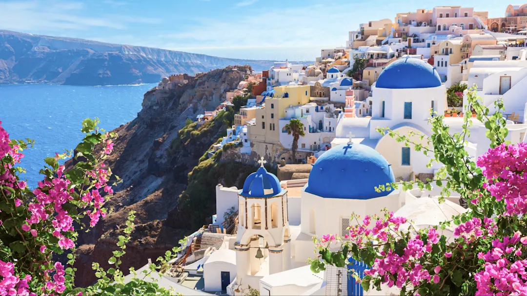 Weiße Häuser mit blauen Kuppeln und Blumen auf Klippe, Oia, Santorini, Griechenland