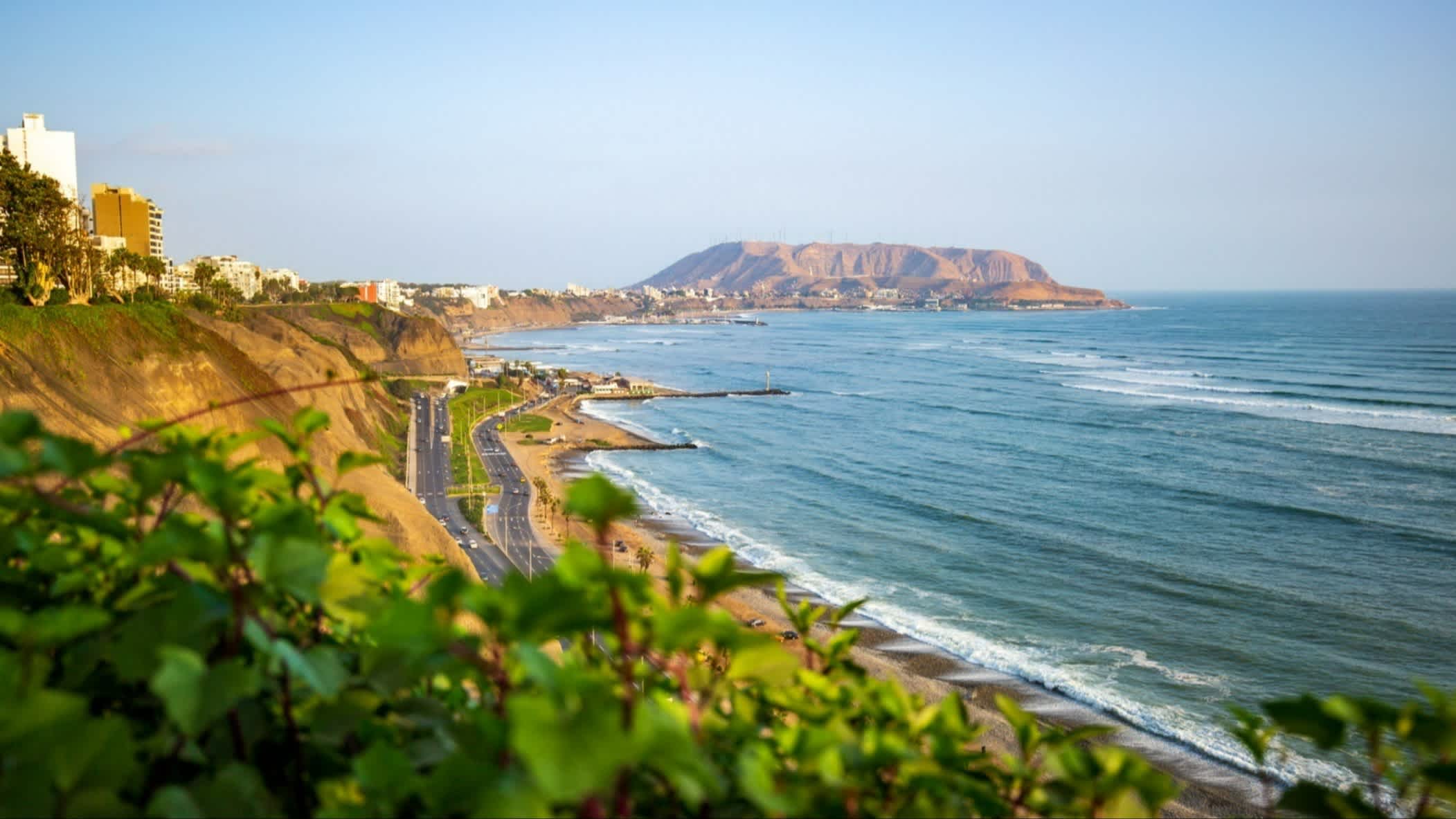 Playa Embajadores bei Lima, Peru mit Vegetation, Häusern, dem Meer sowie Bergen im Bild.