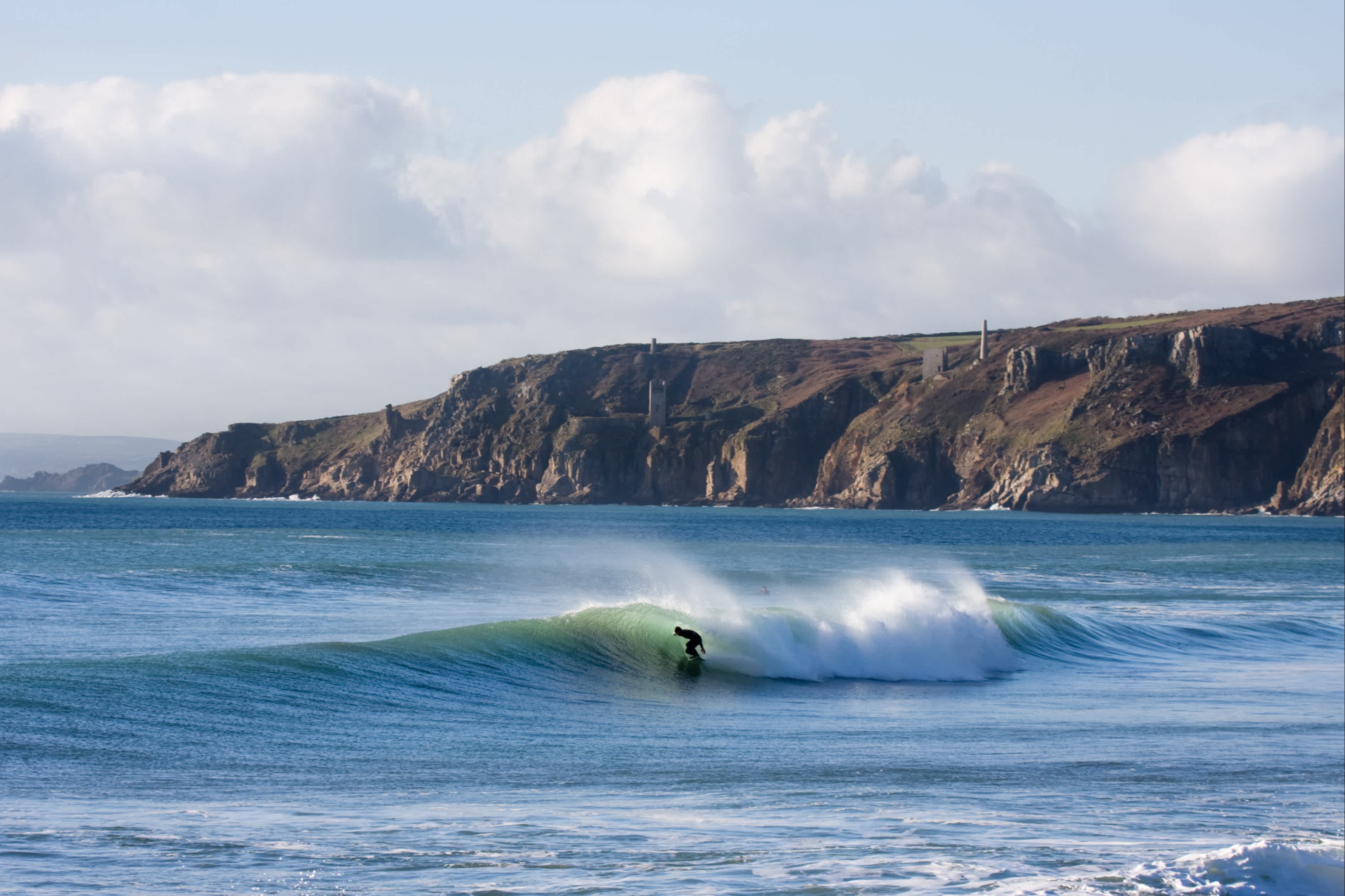 Surfeur sur une vague avec les falaises en arrière-plan, Porthleven, Cornouailles, Angleterre.
